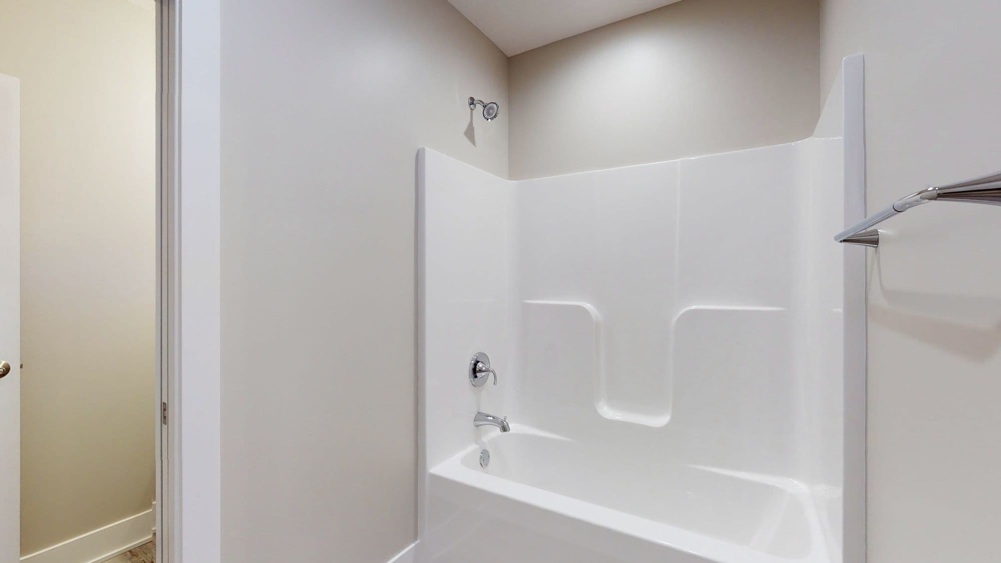 Bathroom features a white bathtub and shower combination with chrome fixtures and a towel bar. The walls are painted a soft white.