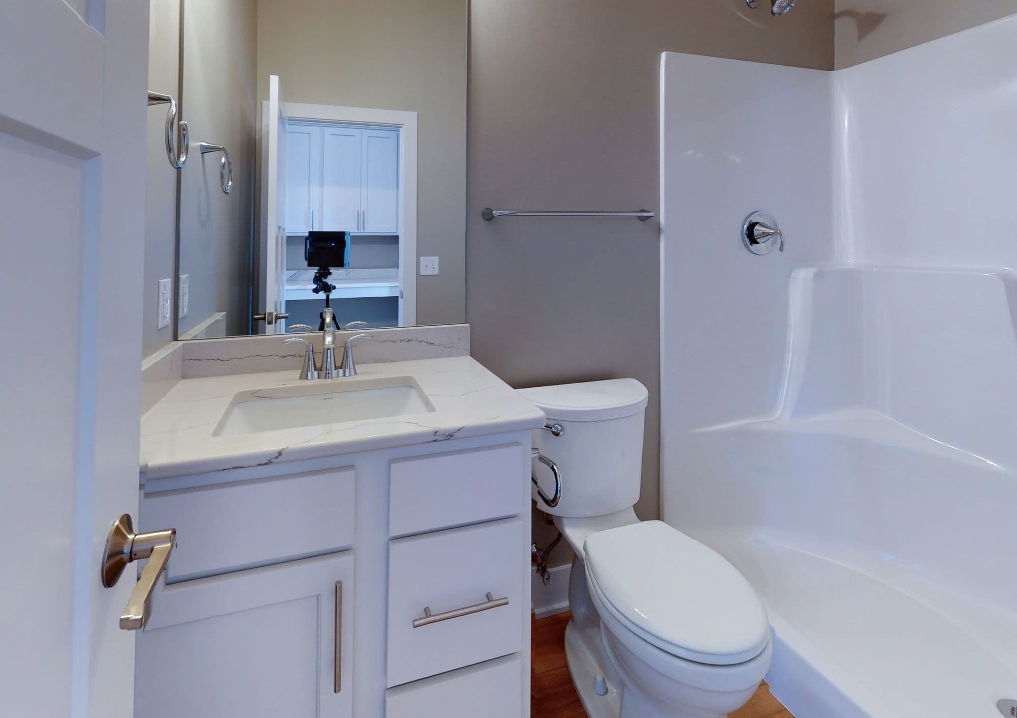 Bathroom with white vanity, toilet, and shower stall. The vanity has a light countertop and silver hardware, while the shower stall is enclosed in white panels.