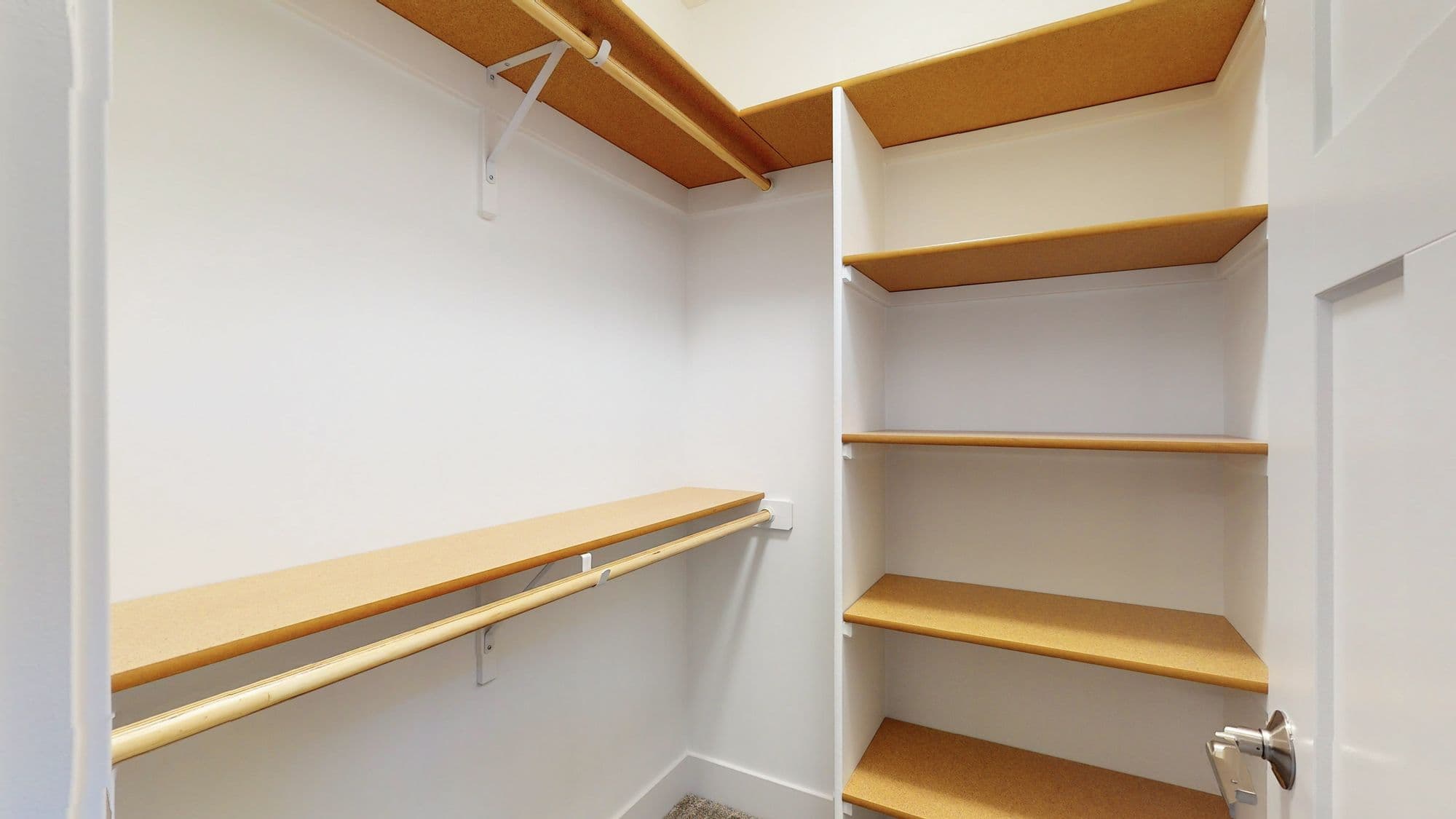 Walk-in closet featuring custom built-in shelving with warm wood tone shelves and a chrome closet rod for hanging clothes. White painted walls with white shelving supports.