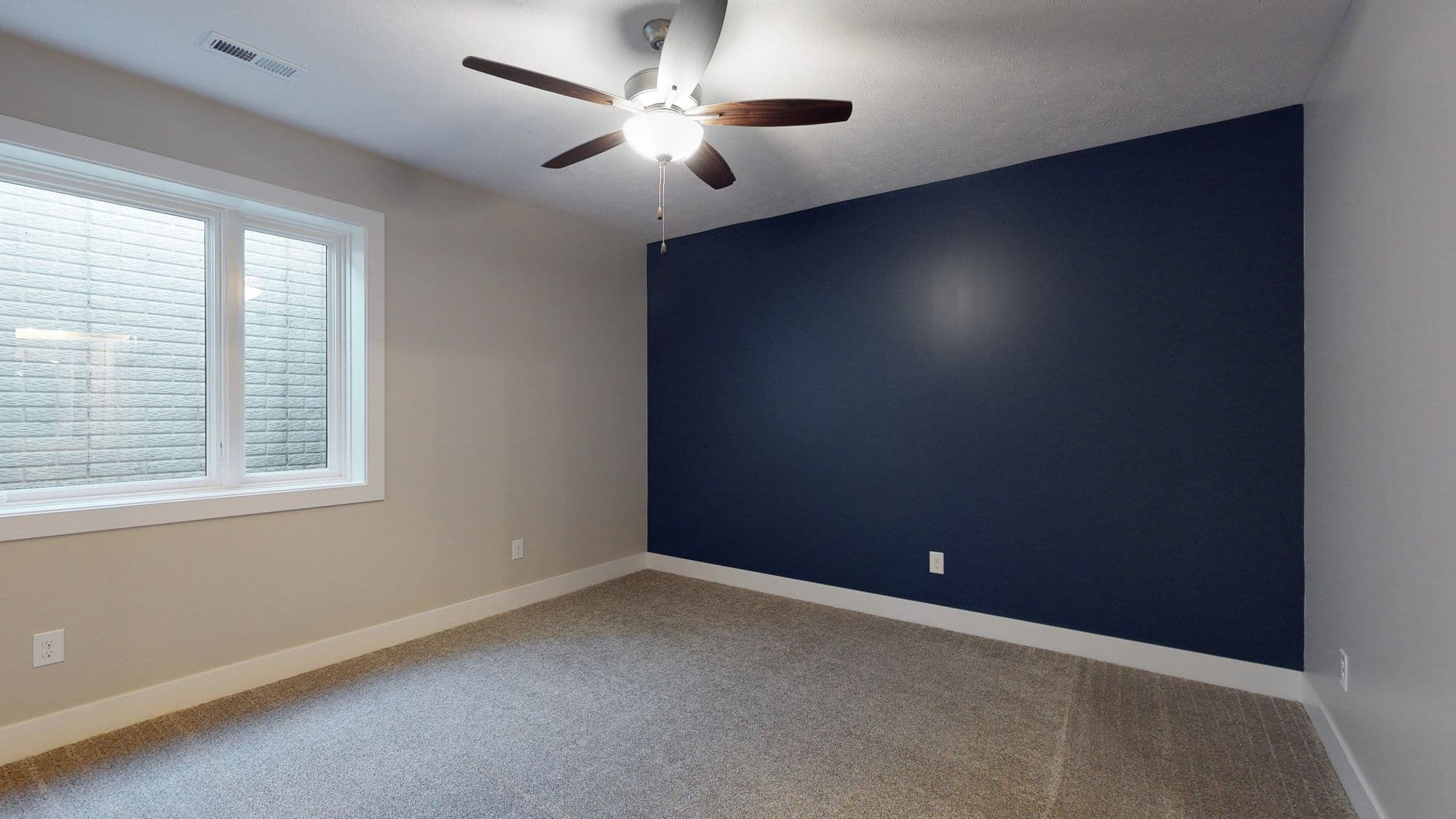 A bedroom features a large window with blinds, a ceiling fan with a light fixture, and a blue accent wall. The flooring is neutral carpet and the room has white trim.