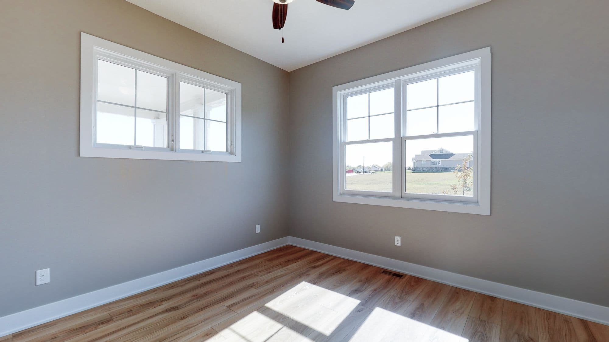 Bright bedroom with wood floors and large windows providing natural light. Neutral wall color and white trim create a clean and modern aesthetic.