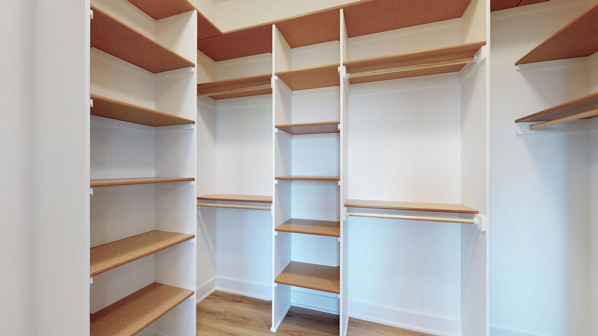 Walk-in closet with built-in white shelving and wooden shelves with wooden clothing rods. Multiple tiers of shelving creates ample storage.