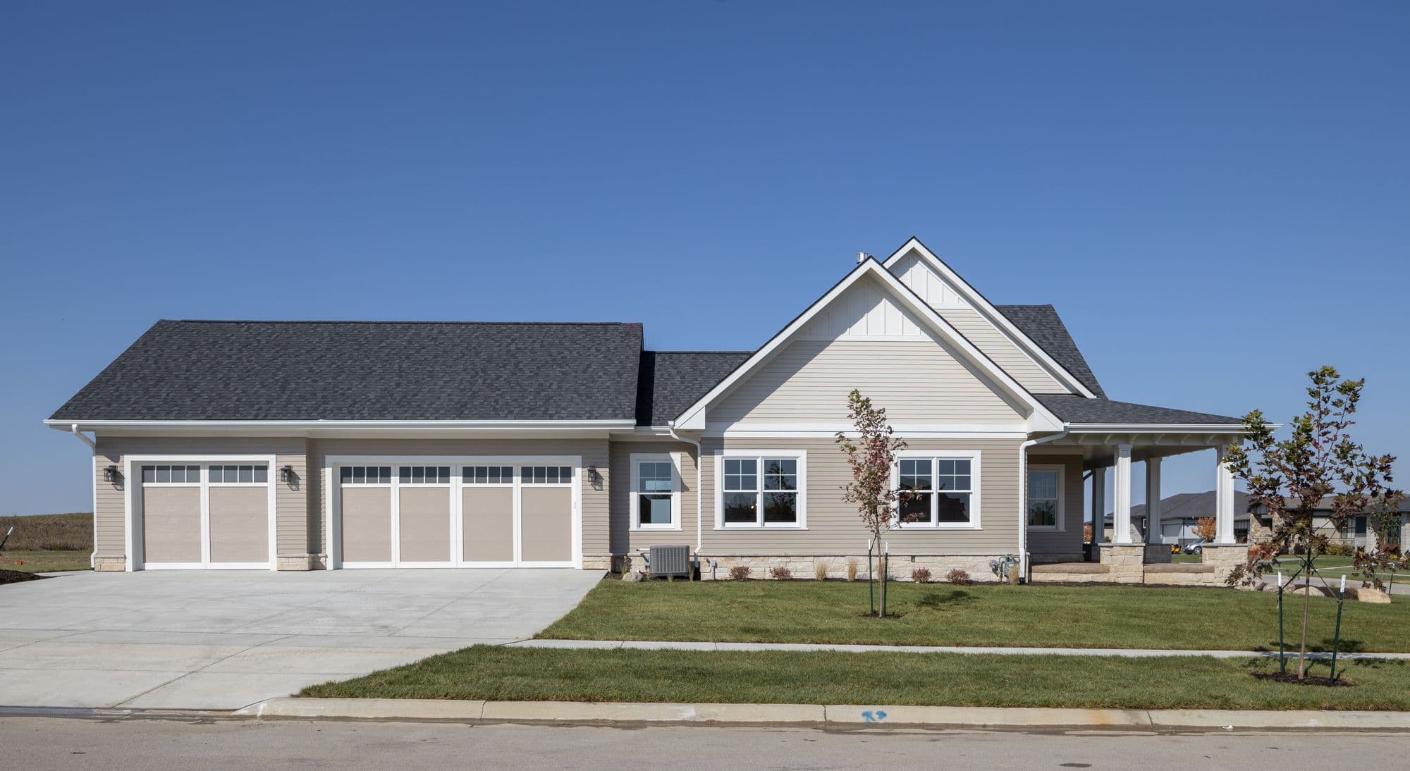 Exterior view of a modern single-story home with a three-car garage. The house features beige lap siding, a gray roof, white trim, and a covered front porch.