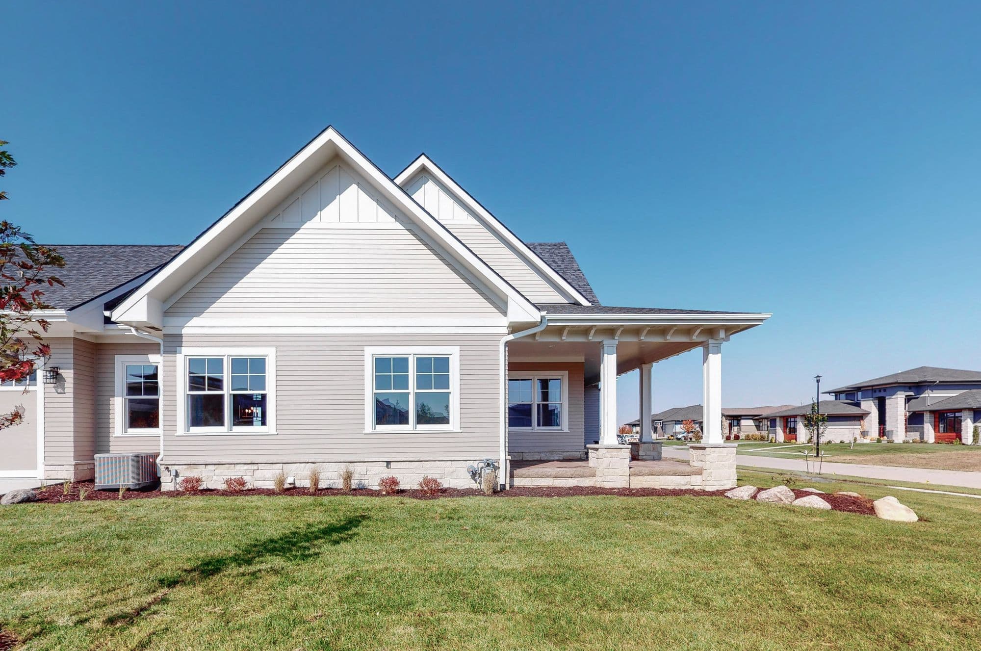Exterior view of a single-story home with light beige siding and a covered front porch with white columns. Well-manicured lawn and landscaping enhance the curb appeal.