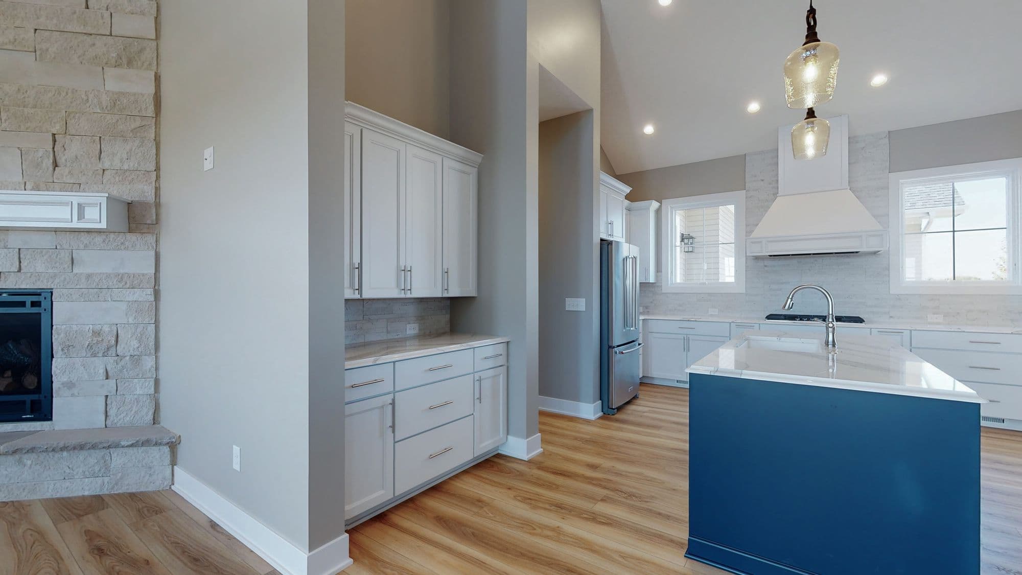 Spacious kitchen with a blue island, white cabinets, and stainless steel appliances. The kitchen also features light wood flooring and a stone fireplace.