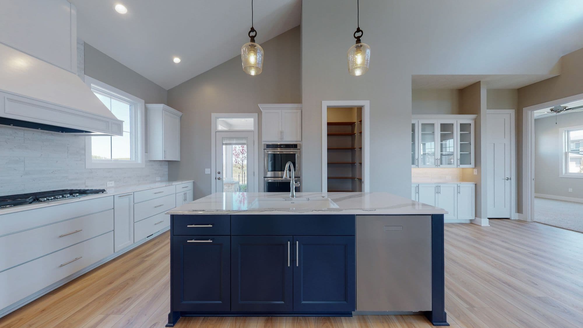 Modern kitchen with white cabinets and navy blue island with marble countertops. Pendant lighting hangs above the island, and stainless steel appliances are visible.