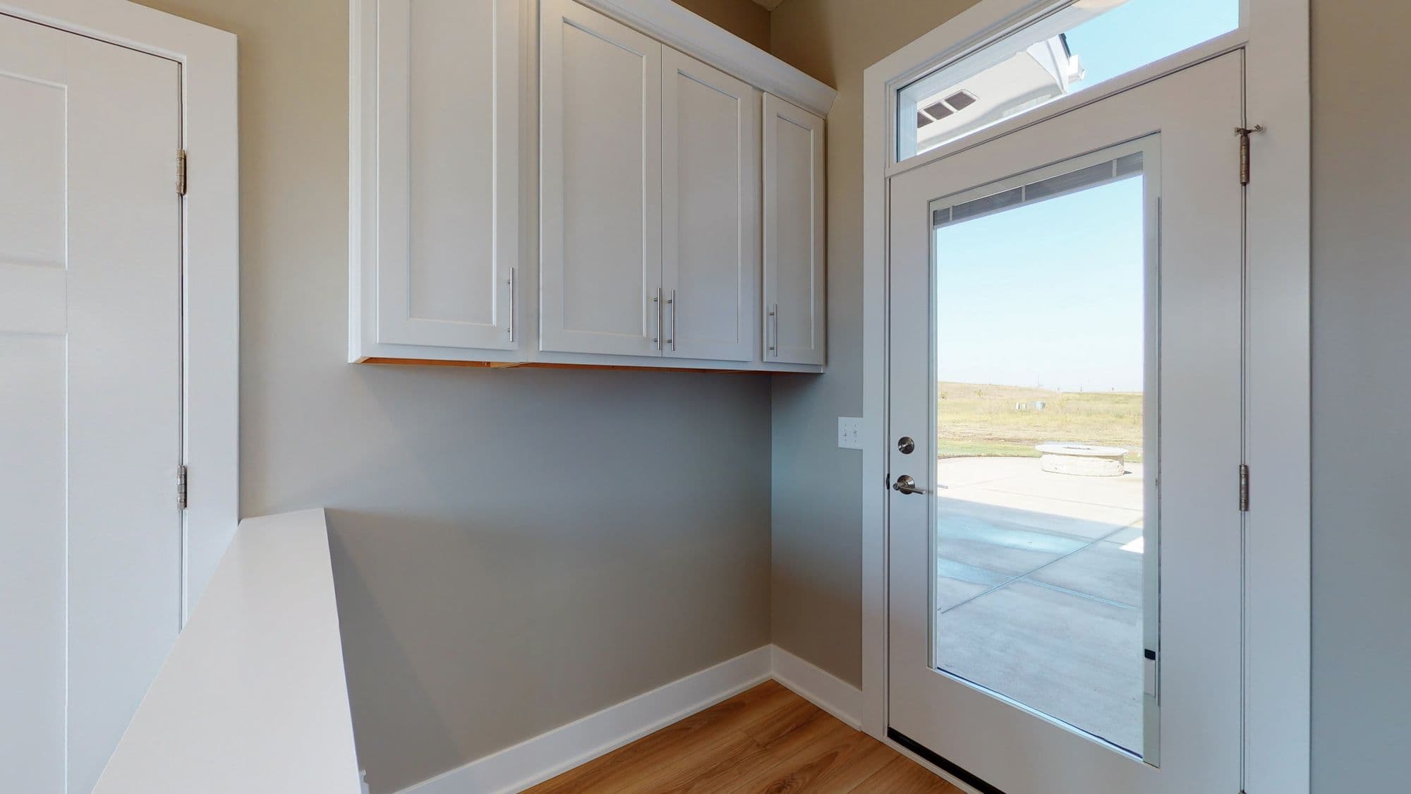 Laundry room featuring white cabinetry and a glass door leading to the exterior. Wood-look flooring and light gray walls complete the space.