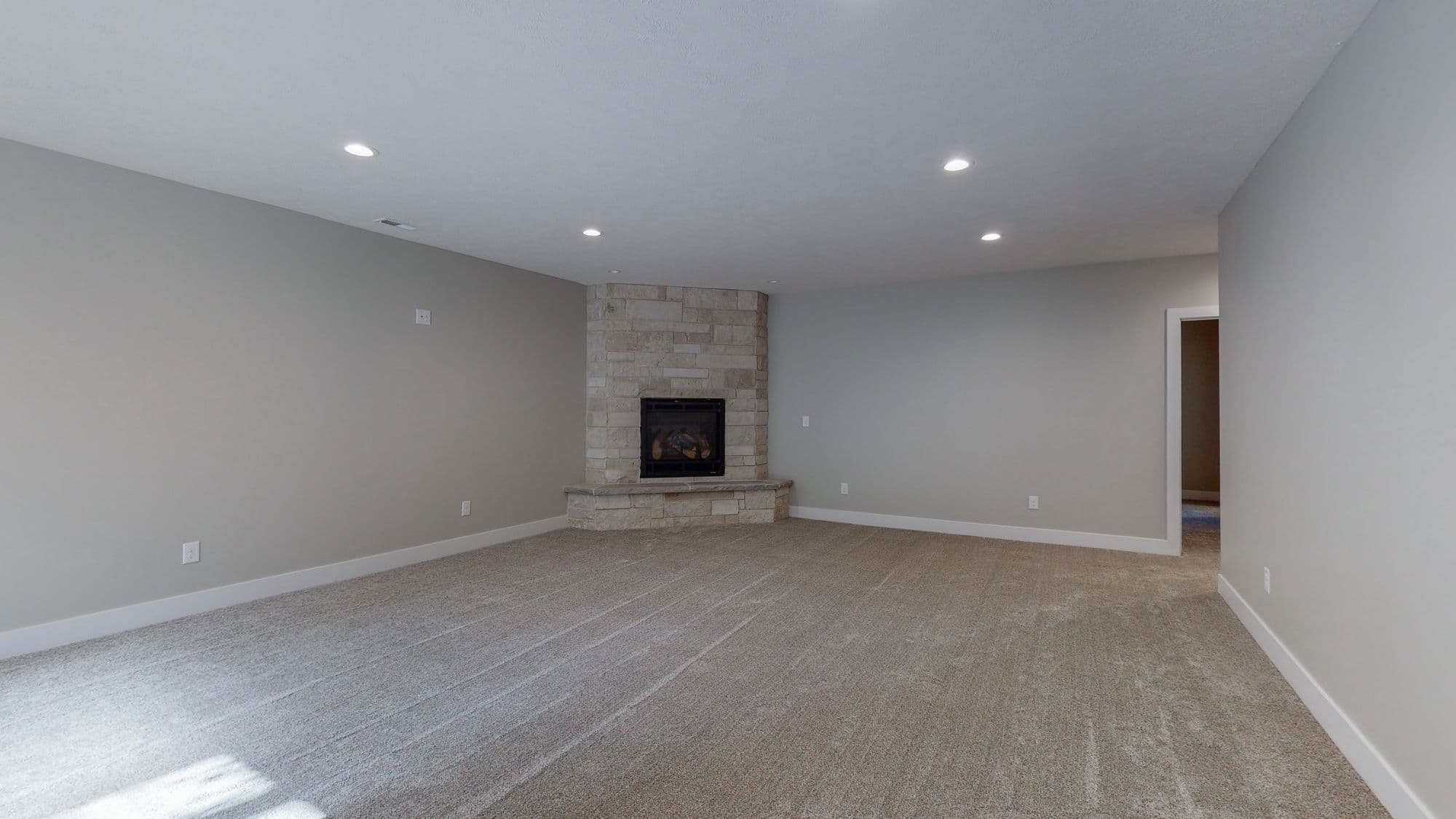 Spacious living room features a stone fireplace, neutral carpeting, and recessed lighting. The walls are painted in a soft gray color and there is white trim throughout the space.