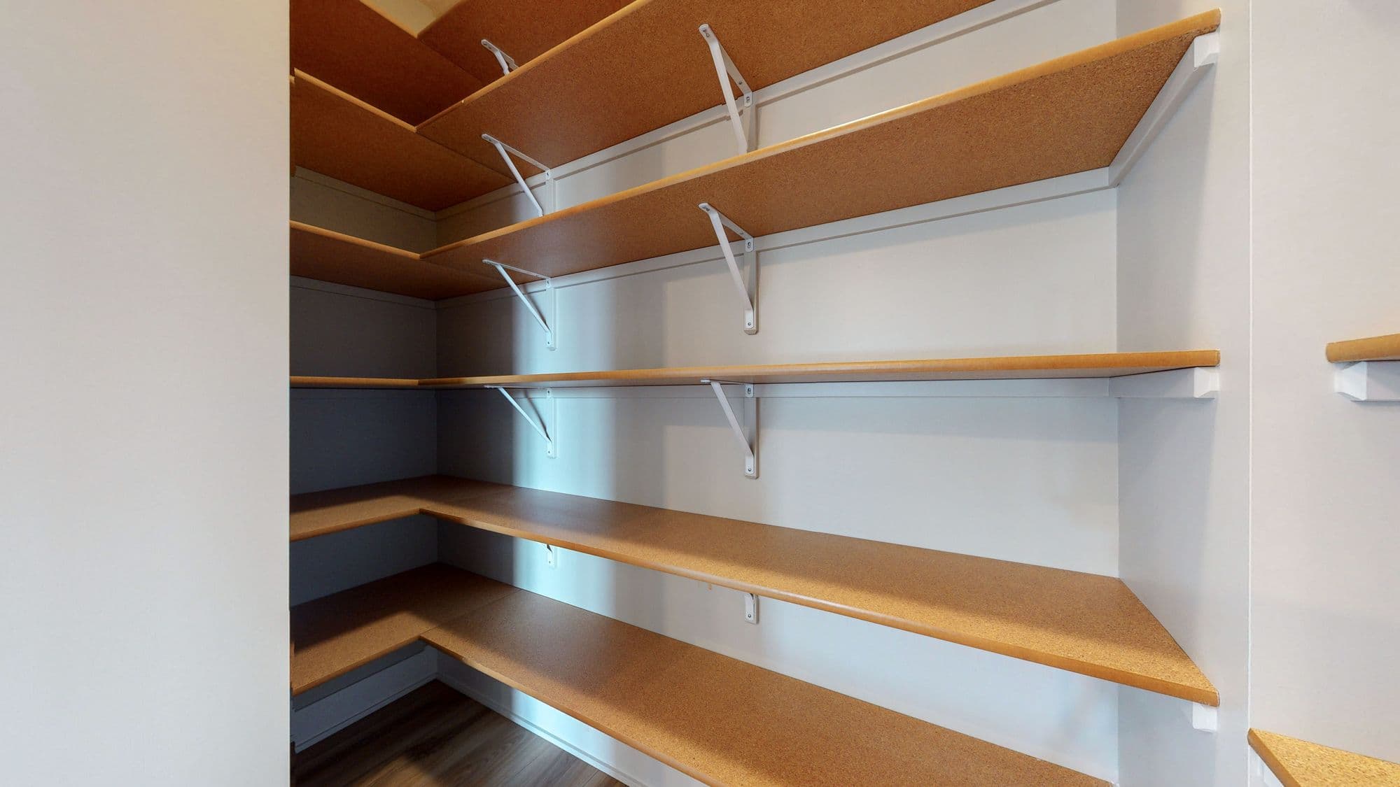 Walk-in pantry with corner shelving. The adjustable shelves are wood-look with white metal brackets.