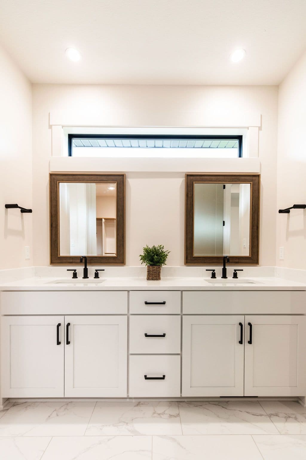 Bathroom features a double vanity with white cabinets, black hardware, and wood-framed mirrors. A small window above the mirrors provides natural light, and the floor is tiled with a marble pattern.
