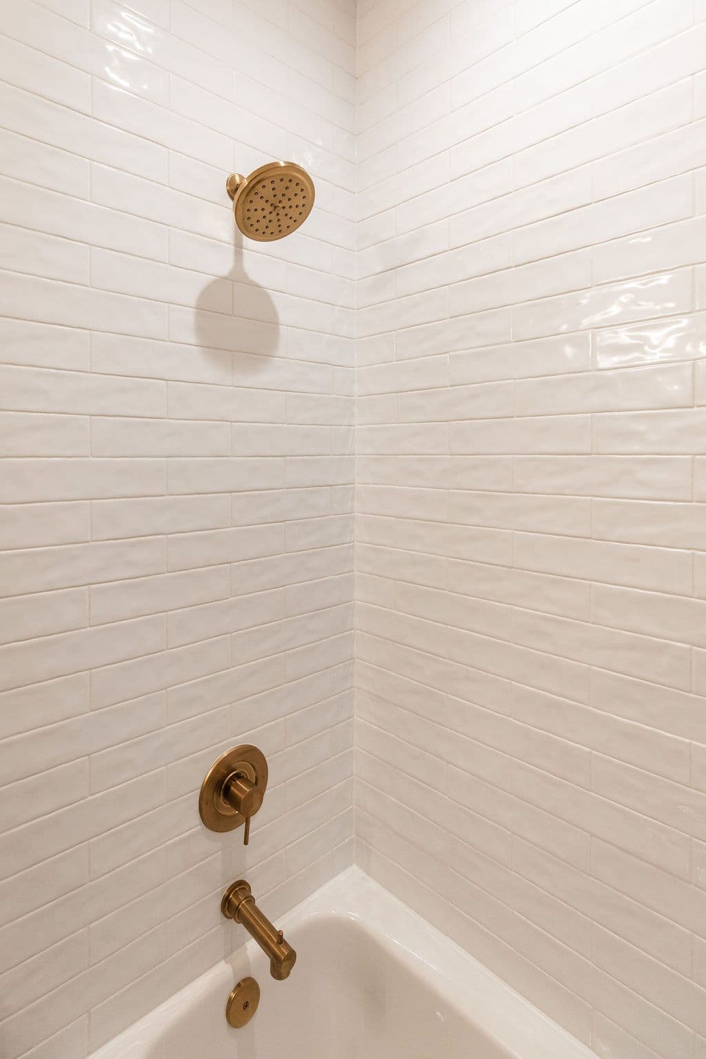 Modern bathroom featuring white subway tile walls, a bronze shower head, and matching bronze faucet fixtures. The bathtub is a clean, bright white.