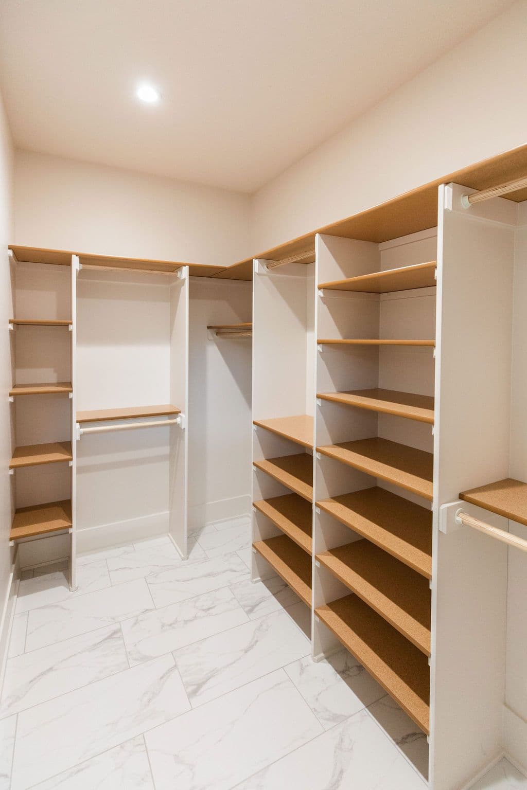 Walk-in closet with custom shelving and hanging rods offers ample storage space. The closet features a combination of open shelving and enclosed storage areas, with the white cabinetry contrasting with the light brown shelves.
