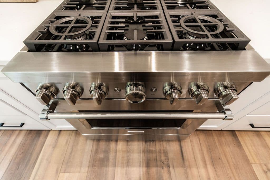Close-up shot of a stainless steel oven and gas cooktop with six burners. The oven features a handle and a glass door.