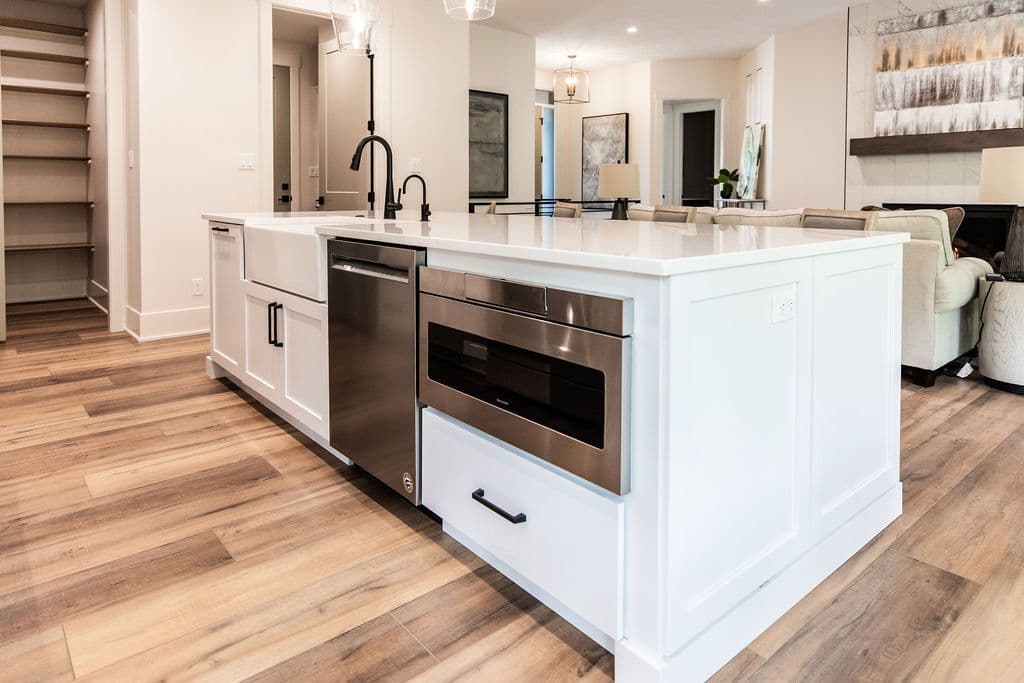 Modern kitchen featuring a large center island with a white countertop and farmhouse sink. Stainless steel appliances and a built-in microwave enhance the space's functionality, complemented by warm wood-look flooring.