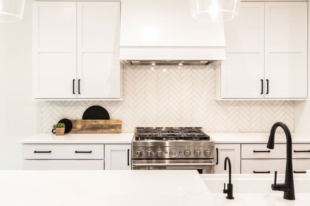 Modern kitchen features white cabinets, countertops, and walls, creating a bright and airy atmosphere. Stainless steel appliances and black hardware add contrast and style.