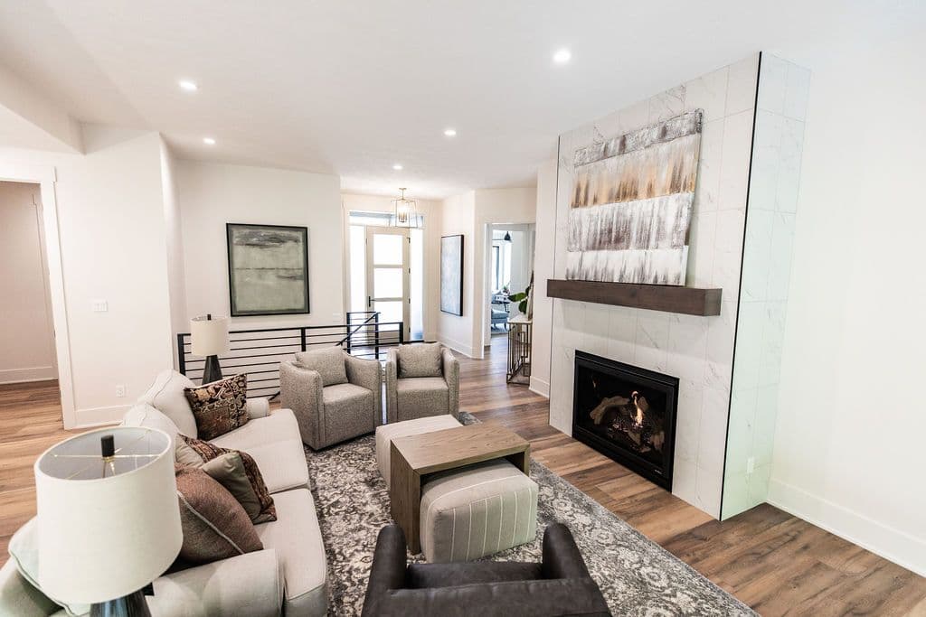 This living room features a tiled fireplace with a wood mantle and abstract art. A sofa, upholstered chairs, and ottoman offer seating on a patterned rug.