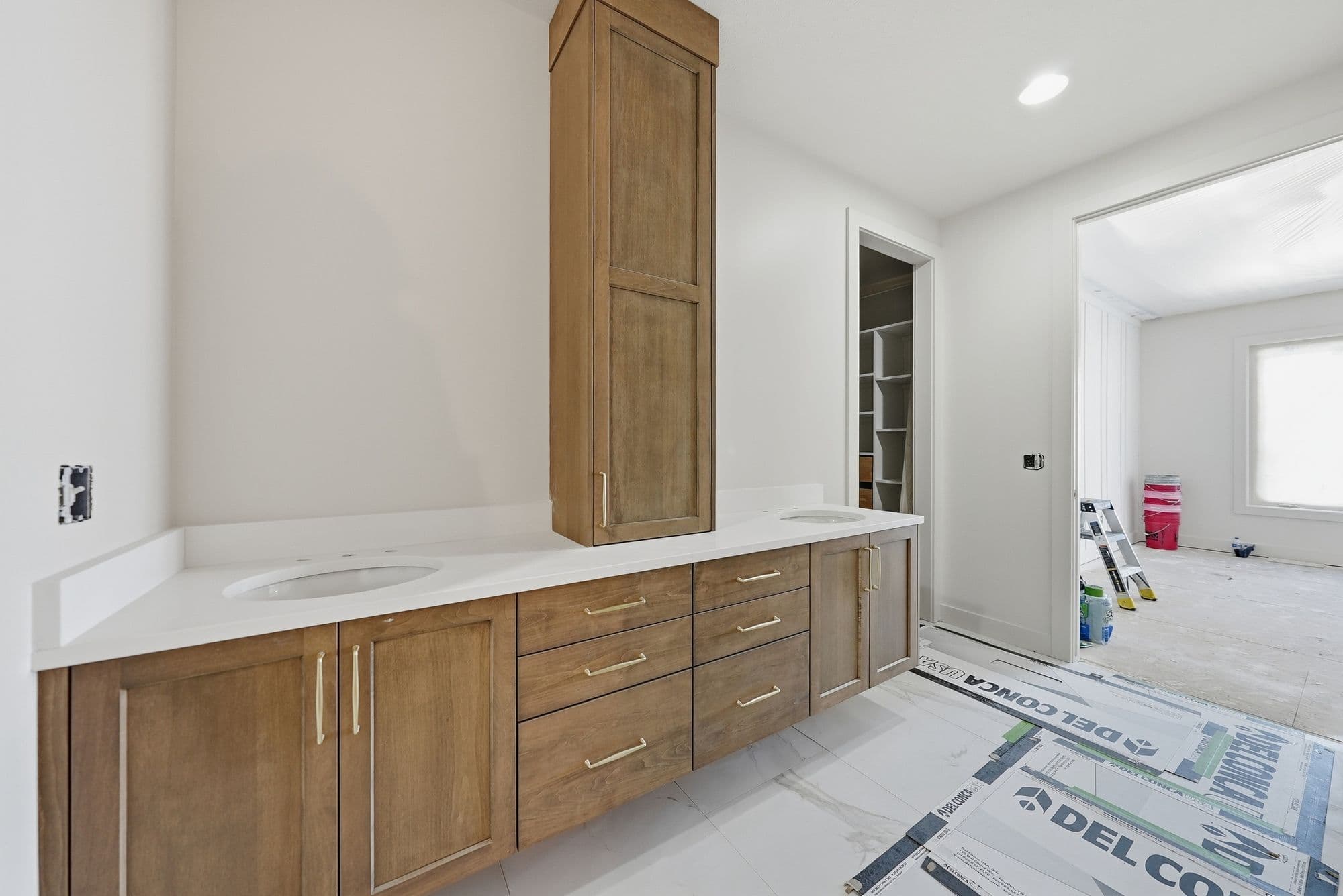 Modern bathroom with wood-toned vanity and white countertop. Features include a tall cabinet and double sinks.