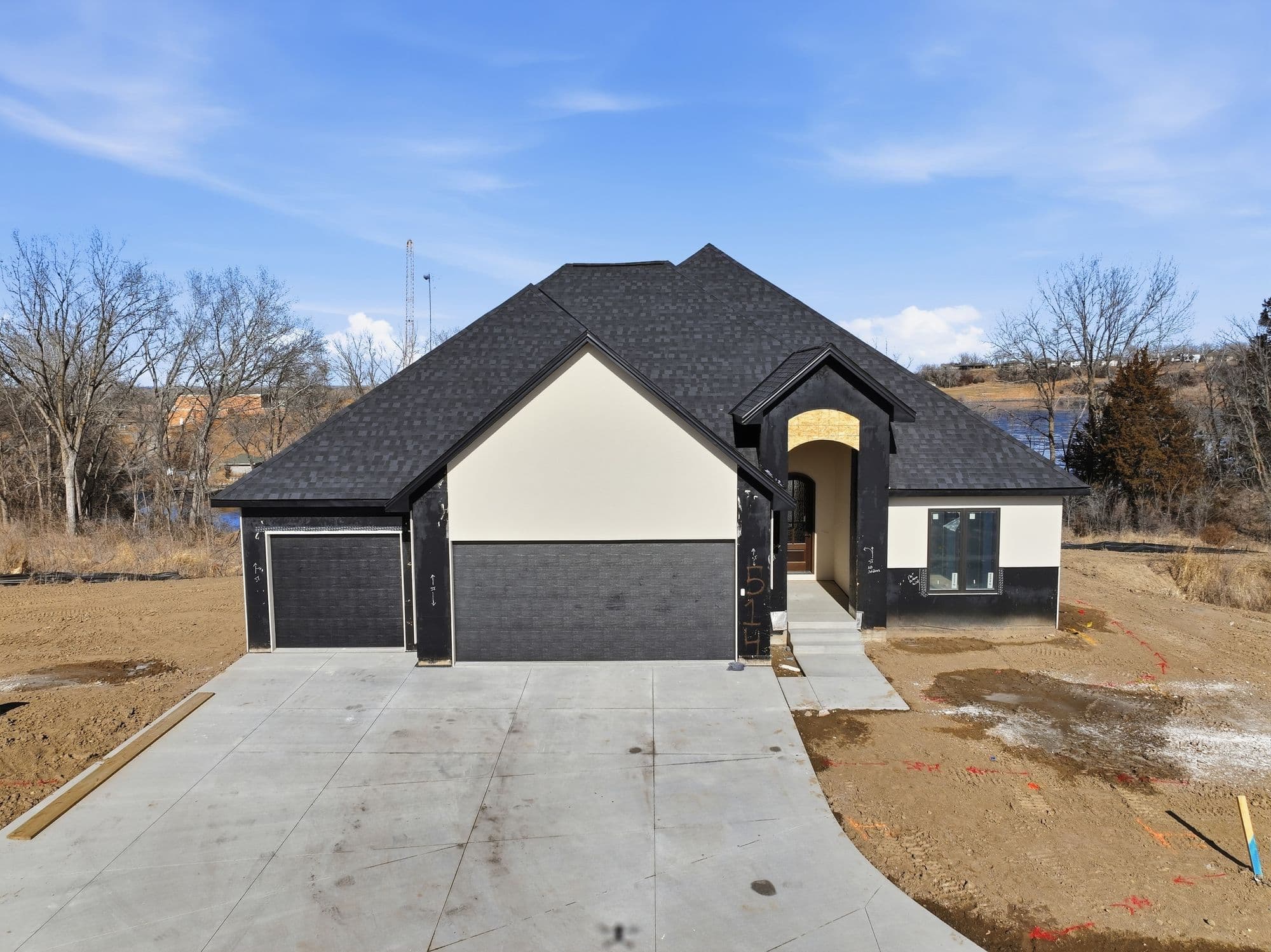New construction home with black accents, including garage doors, trim, and roofing. A concrete driveway leads up to the two-car garage, and the landscaping is still in progress.