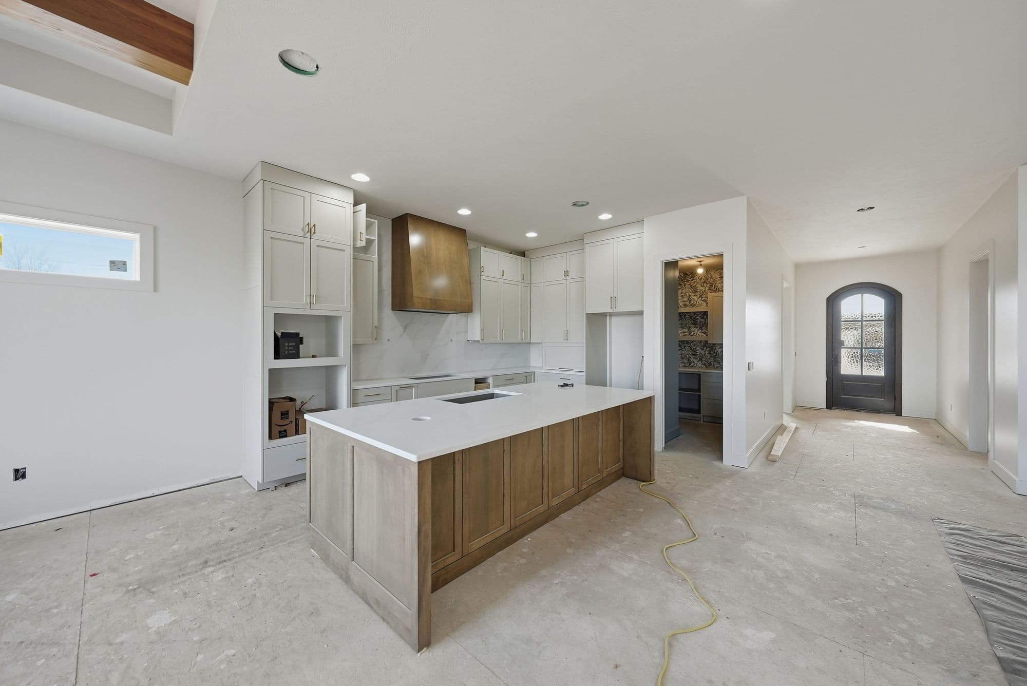 Kitchen area with white cabinets, wood island, and open floor plan. The kitchen features a large island with a white countertop, stainless steel appliances, and a wood range hood.