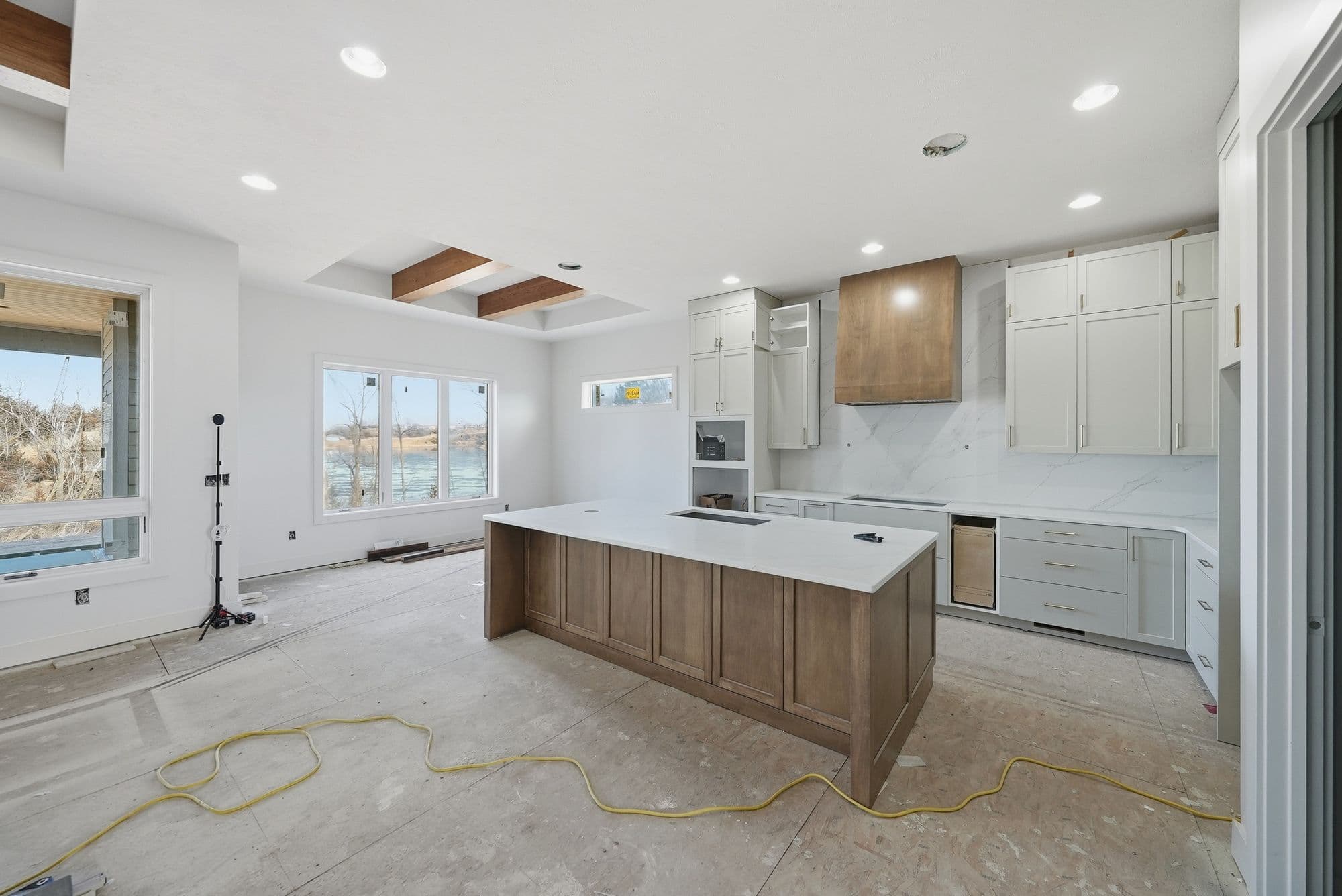 Modern kitchen with light gray cabinets, wooden island, and white countertops. The room is bright with natural light from a large window overlooking a water feature.