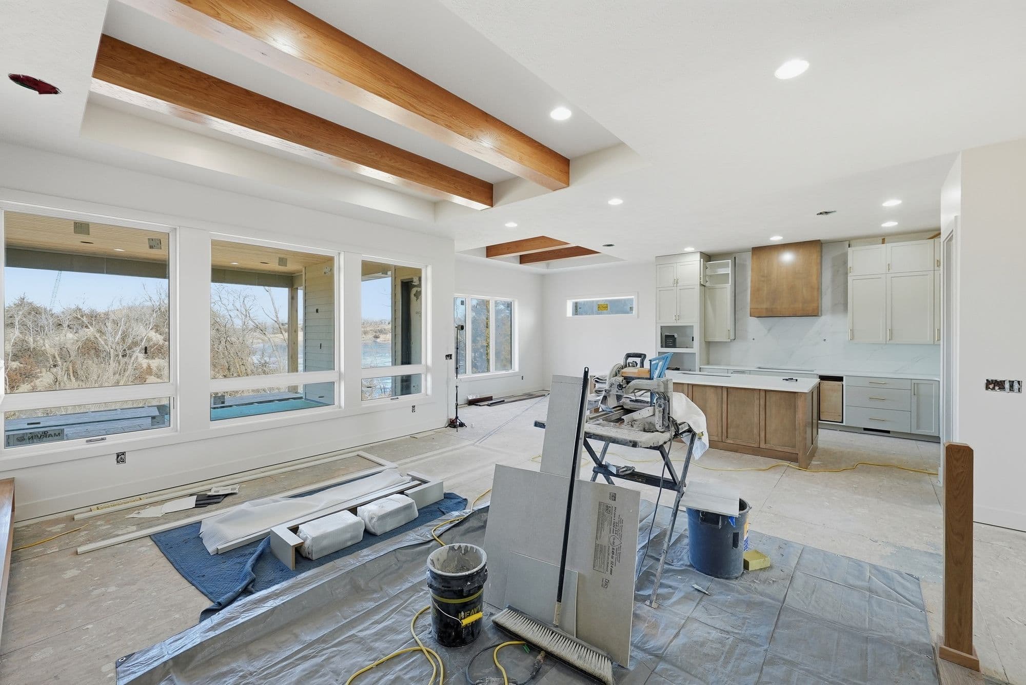 Under construction modern kitchen with hardwood floors and many large windows. New cabinets and countertops are installed but floors are not yet completed.