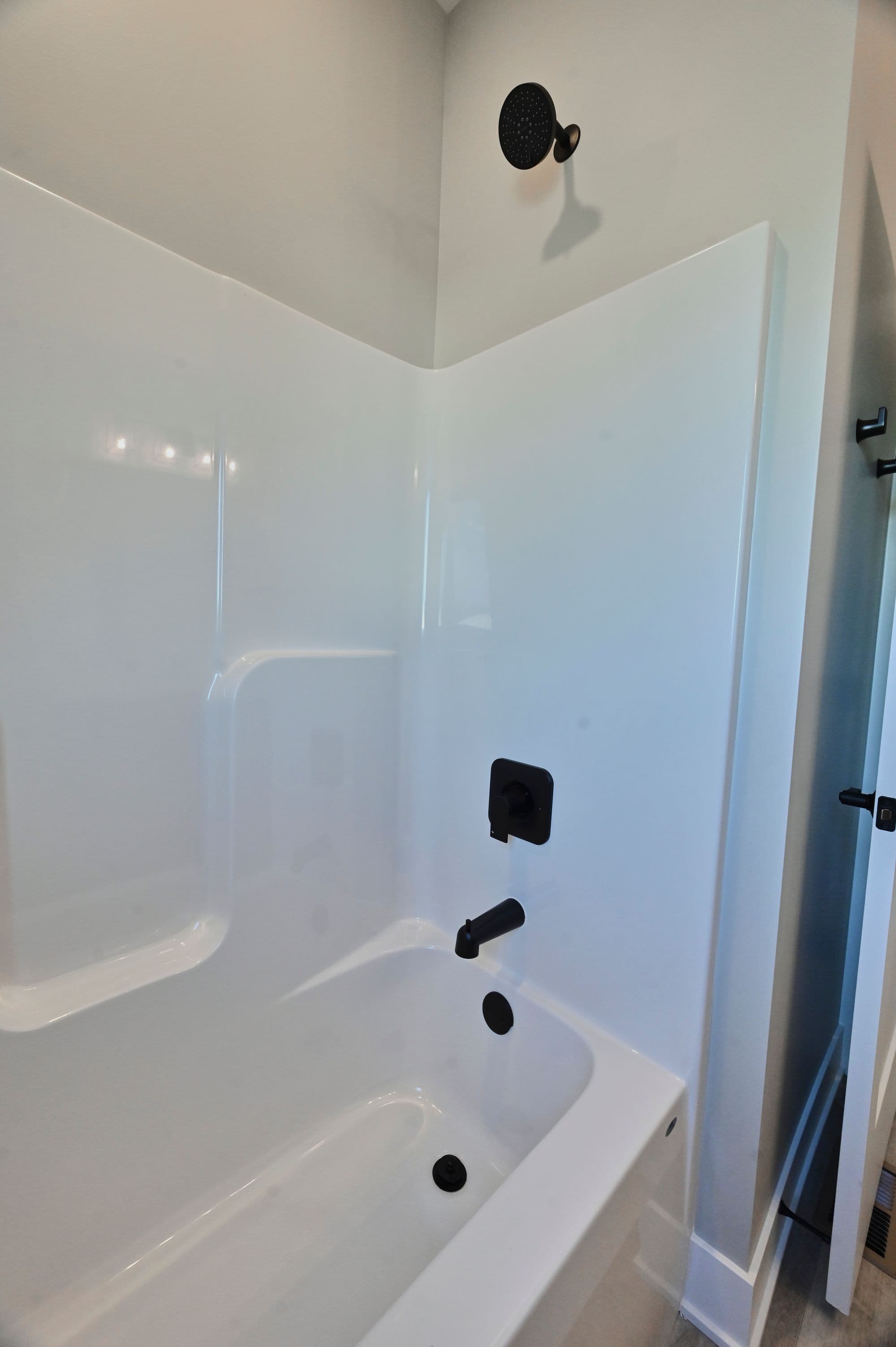 Bright white bathroom features a bathtub with integrated shower surround. The shower has matte black fixtures including a rain shower head and faucet controls.