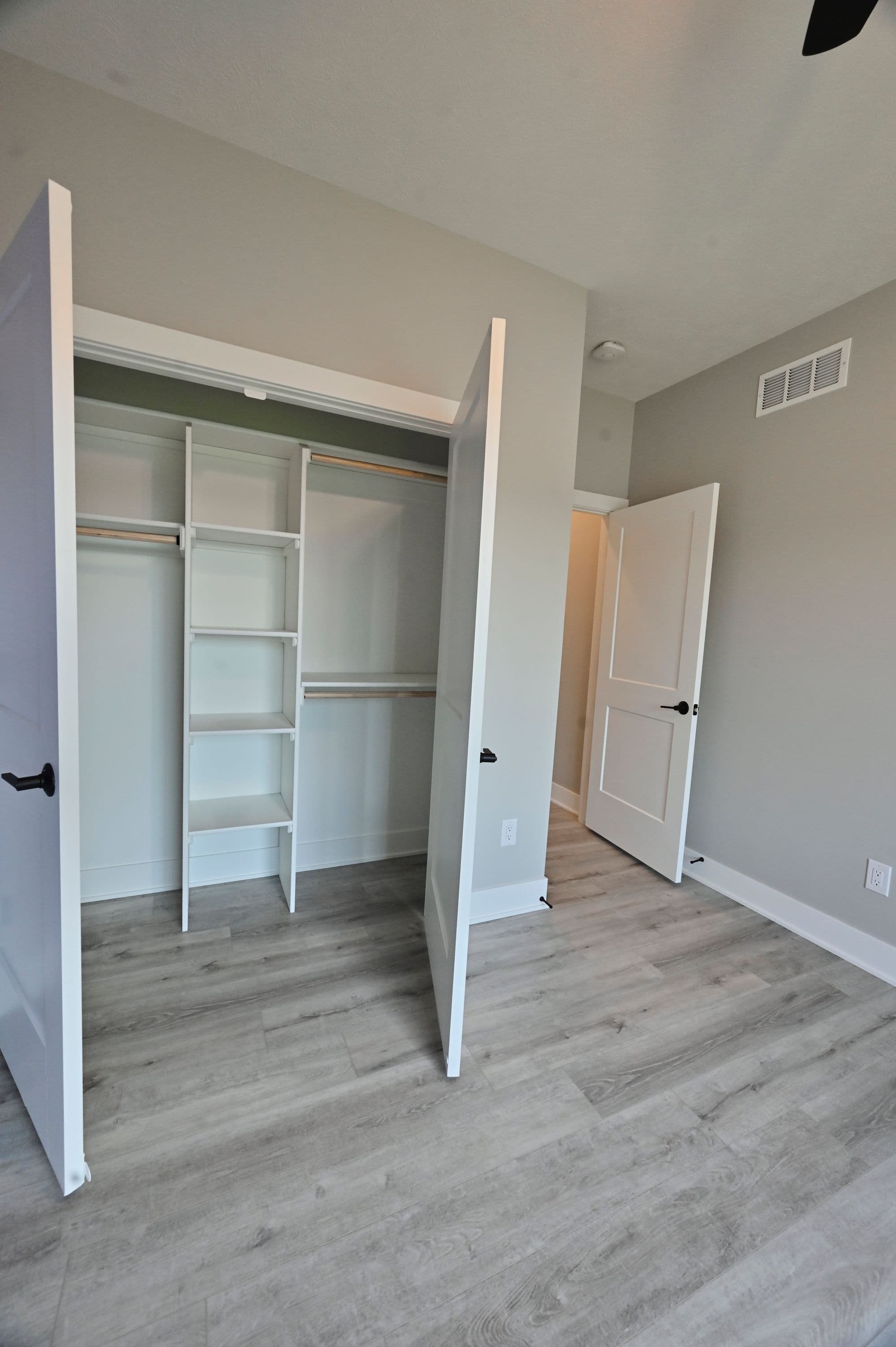 Bedroom with closet featuring open shelving and hanging rods, accompanied by a doorway leading into the room. The space is finished with light wood-look flooring.