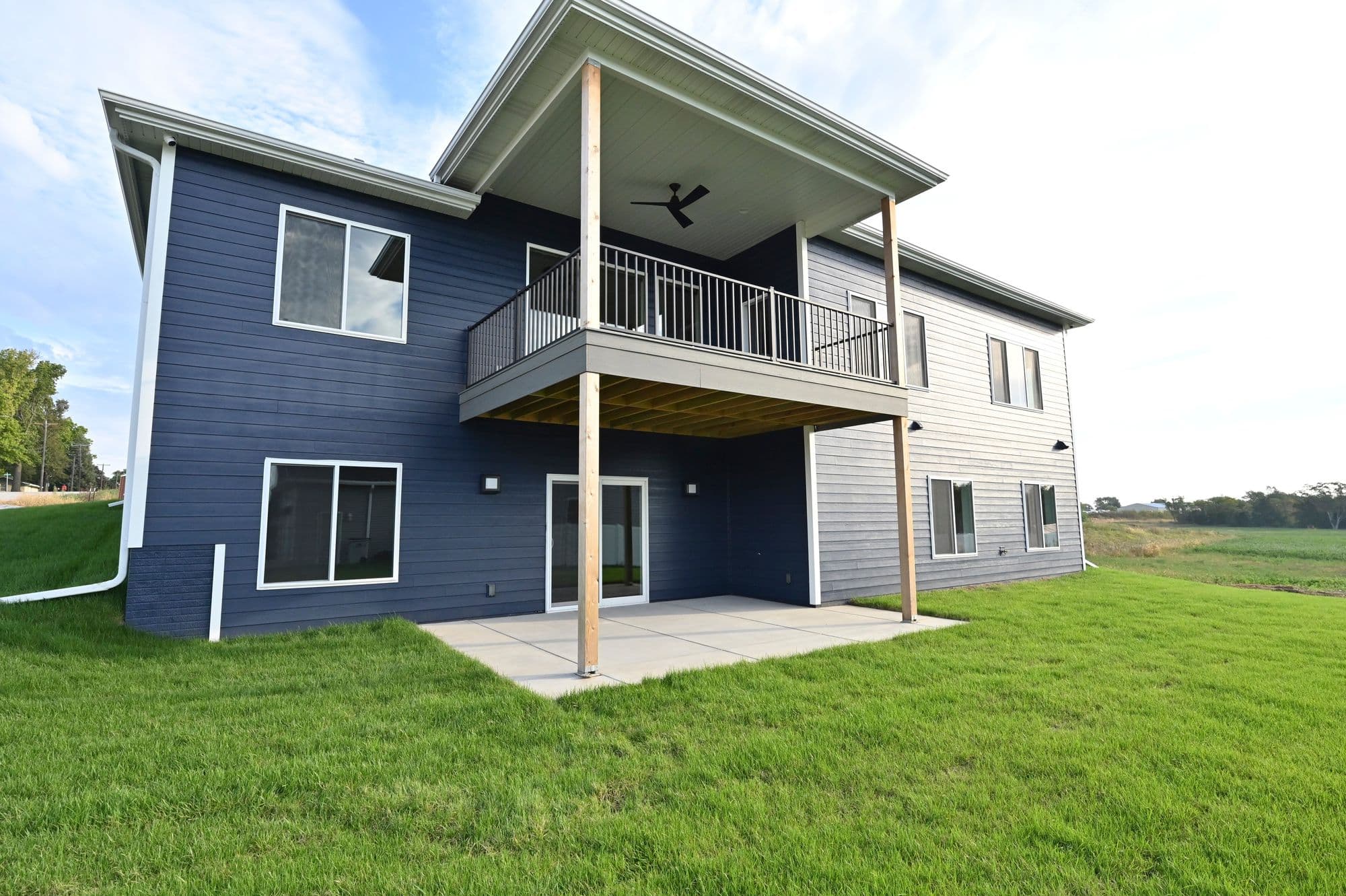 Two-story home with navy blue and light gray horizontal siding and a covered deck. The deck features black metal railings and natural wood posts.