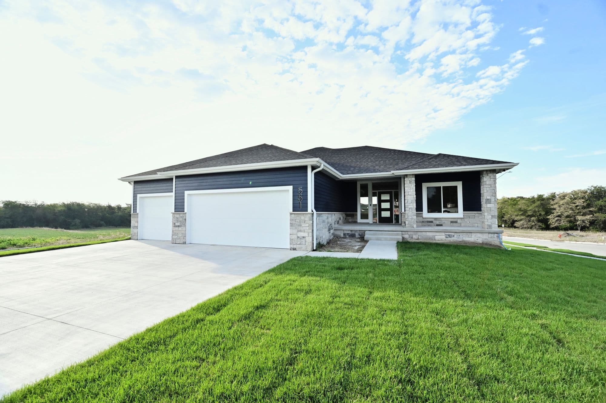 Contemporary home with a two-car garage, stone accents, and horizontal siding. A well-manicured lawn and concrete driveway add to the curb appeal.
