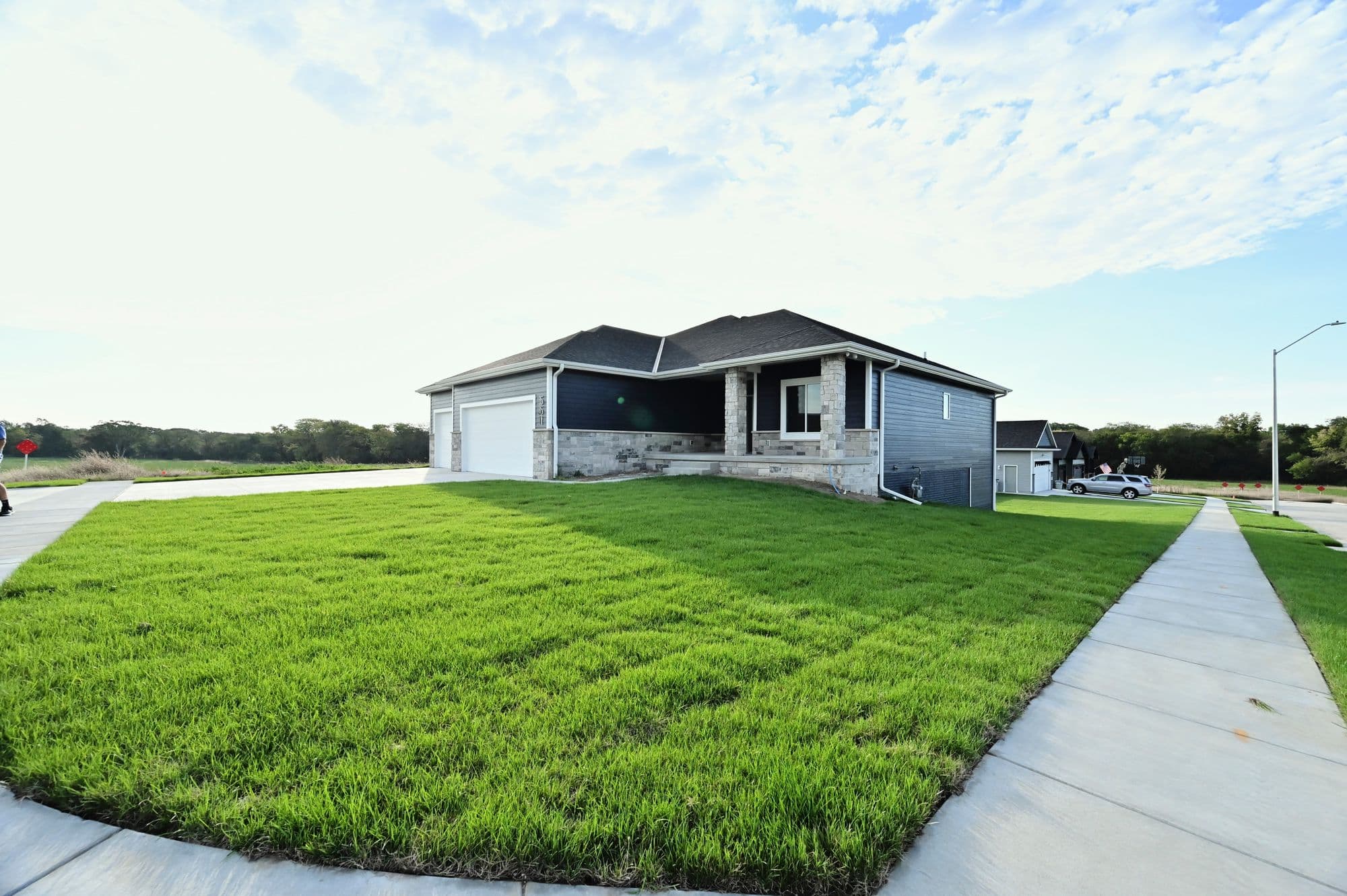 Exterior shot of a single-story home with navy blue siding, stone accents, and a well-maintained green lawn. A concrete walkway leads to the street, and a two-car garage is attached to the house.