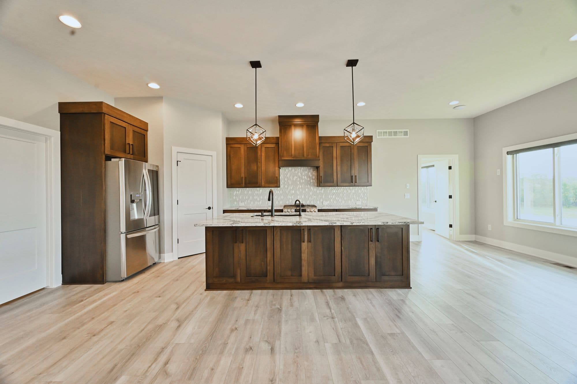 Spacious kitchen featuring dark wood cabinetry, stainless steel appliances, and a marble island. The kitchen has light wood flooring and recessed lighting throughout.