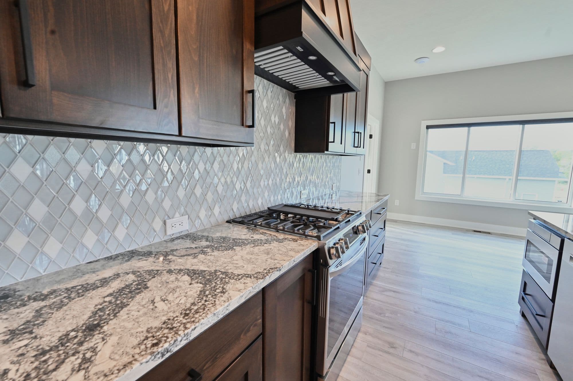 Kitchen featuring diamond-patterned backsplash and granite countertops. Stainless steel stove and range hood complement the dark wood cabinetry.