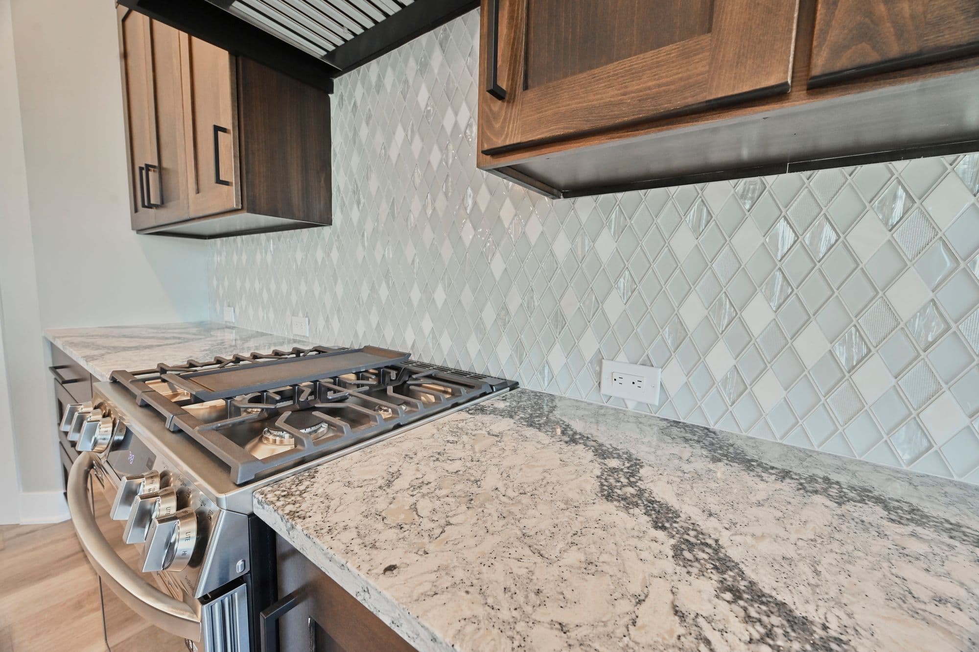 Modern kitchen featuring granite countertops, stainless steel appliances, and diamond pattern backsplash. Dark wood cabinets provide ample storage above the gas range.