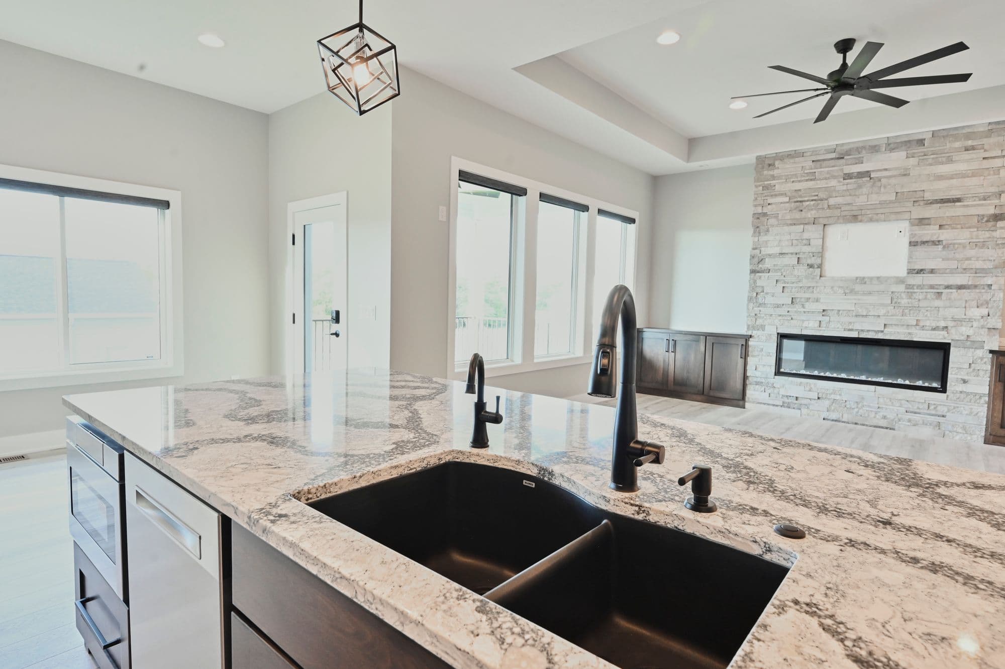 Modern kitchen boasts granite countertops, a black sink with matte black faucet, and stainless steel appliances. The open-concept space includes a fireplace and ceiling fan in the living room.