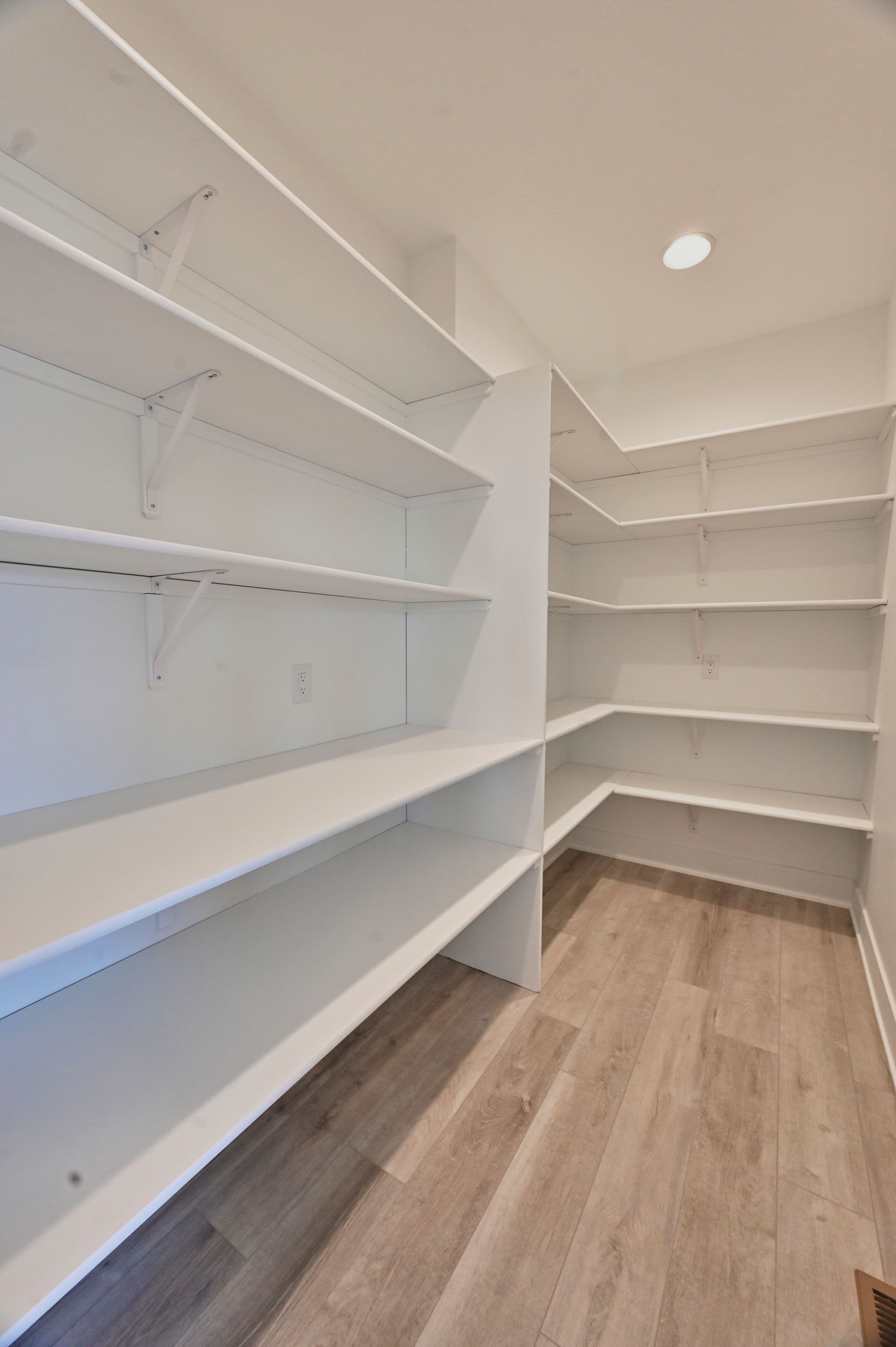 Spacious white pantry with open shelves and wood-look flooring. Abundant shelving provides ample storage in this organized space.