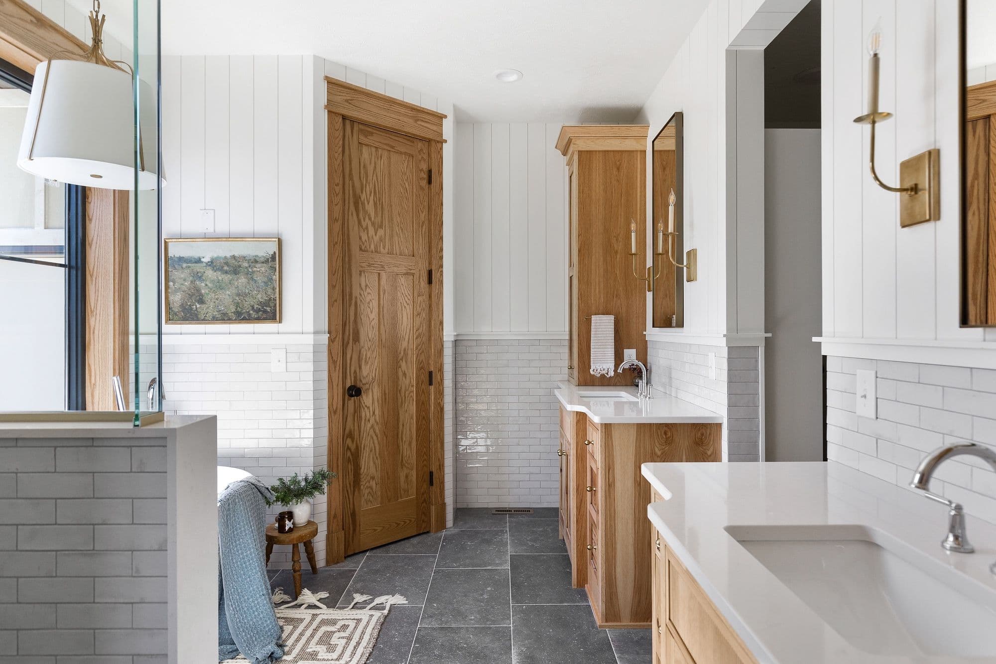 Bathroom featuring a wooden vanity, a white countertop with sink, and a subway tile backsplash. A wooden door is open and the walls are paneled with white boards.