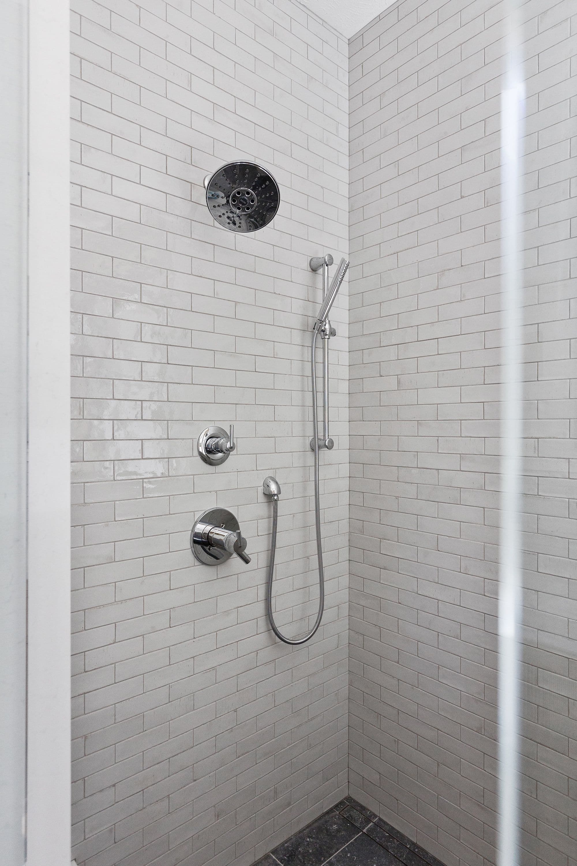 Modern shower features white subway tile walls with gray grout. Chrome fixtures include a rainfall shower head, handheld shower, and temperature controls.