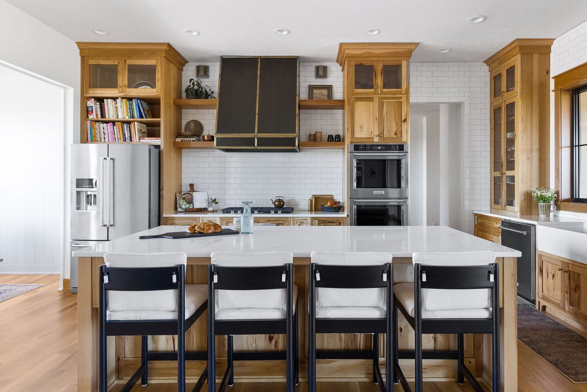 Bright kitchen with natural wood cabinetry, a white quartz island with seating, and stainless steel appliances. Black range hood and white subway tile complete the modern design.