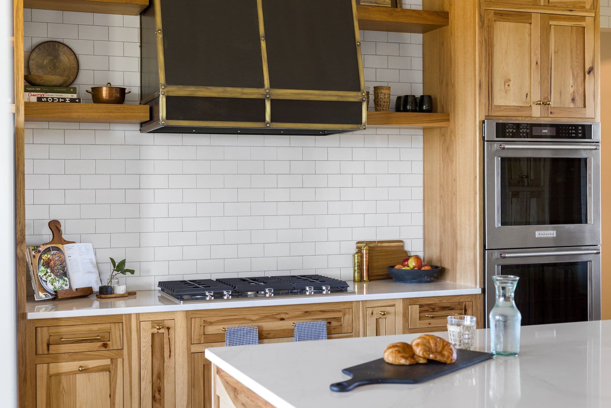 Contemporary kitchen features light wood cabinetry, a white subway tile backsplash, and stainless steel appliances. An island with a white countertop adds additional prep space.
