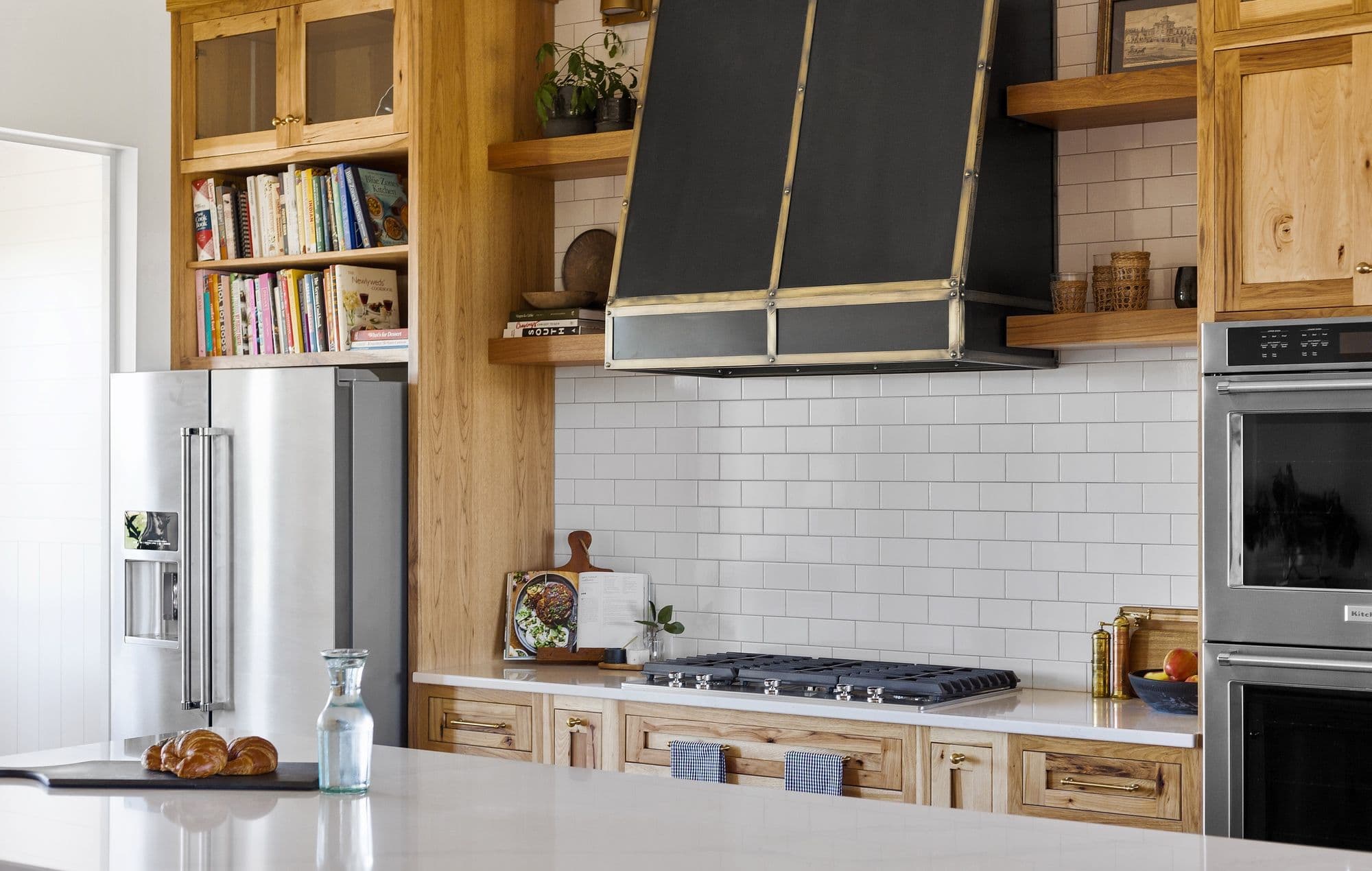 Bright and modern kitchen with stainless steel appliances and custom wood cabinetry. Features include a black range hood, white subway tile backsplash, and a large island with white countertop.