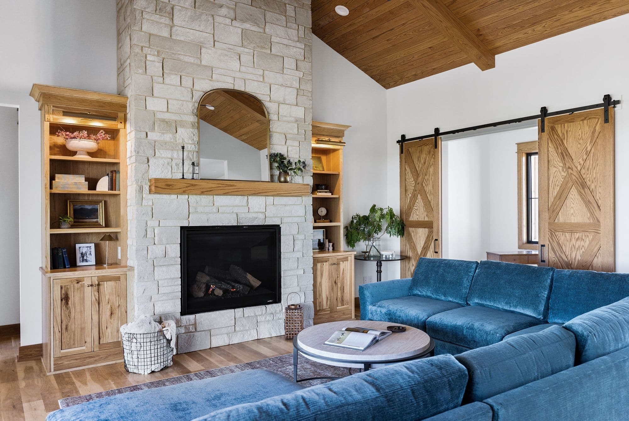 Living room features a stone fireplace with a wooden mantel and an arched mirror. Built-in wooden shelves flank the fireplace, and a large blue sectional couch sits in front of the fireplace.
