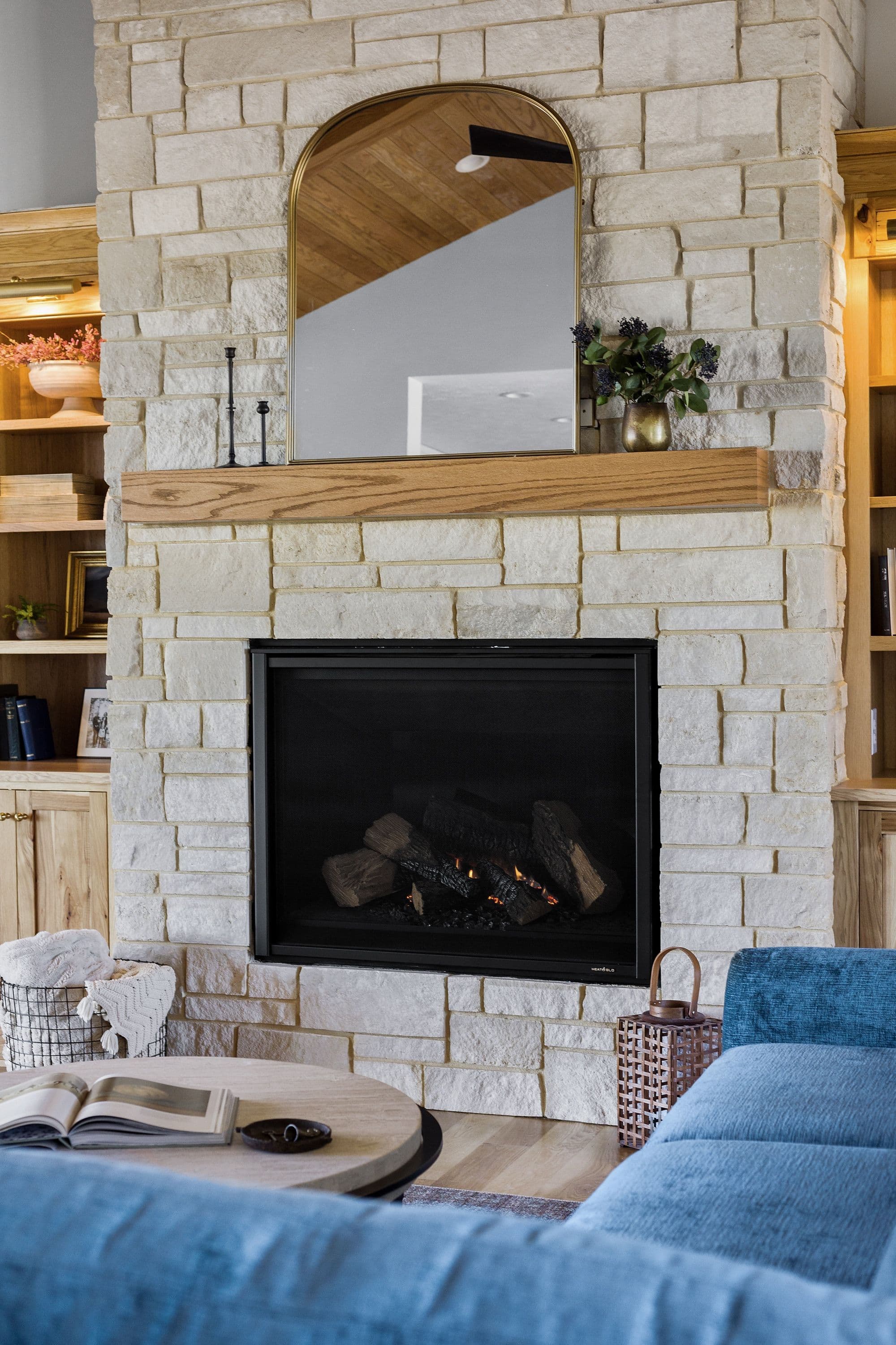 Living room area featuring a fireplace with light stone surround and a wooden mantel. Above the mantel is an arched mirror reflecting part of the room, with built-in shelves on either side of the fireplace.