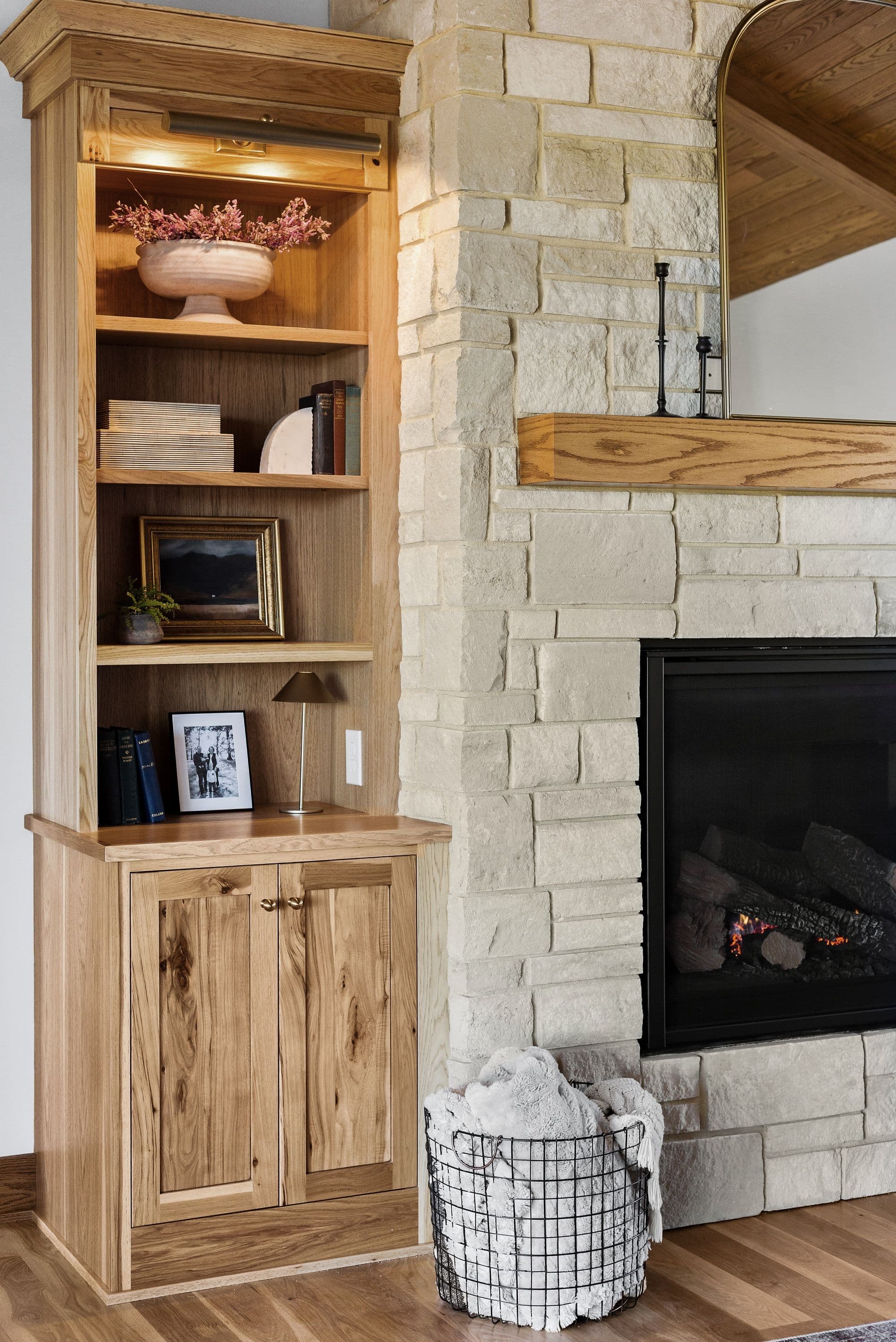 Living room featuring built-in wooden shelving unit and a stone fireplace. The shelving unit contains decorative items and the fireplace is flanked by stone blocks and has a black firebox.