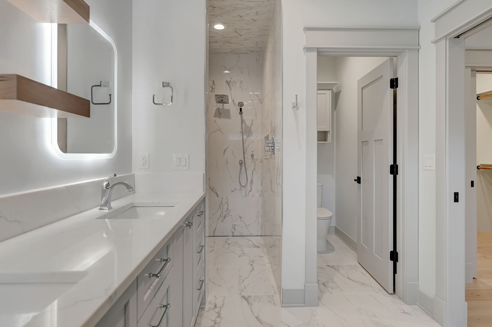 Modern bathroom with white marble tile floors and shower surround. A gray vanity features a white marble countertop and square sink.