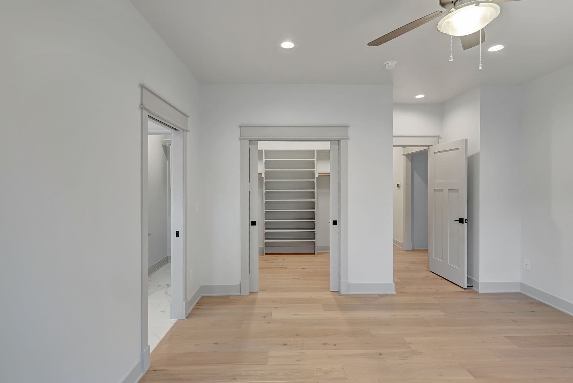 Bright bedroom with hardwood floors and white walls. The bedroom has multiple doorways, one leading to a closet with built-in shelving.