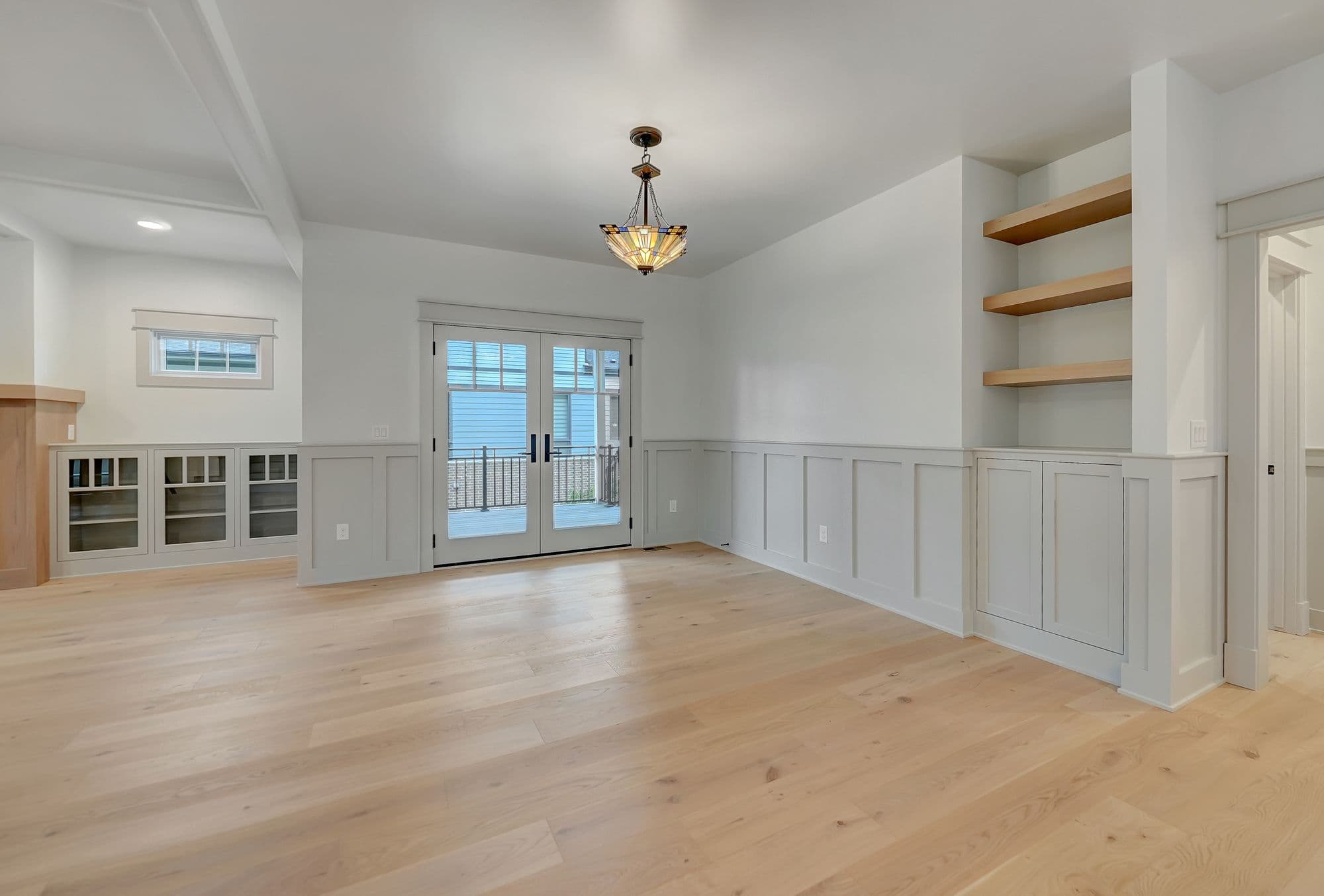 Bright dining room features light wood flooring, white wainscoting, and a chandelier. Glass paneled doors lead to a balcony area.