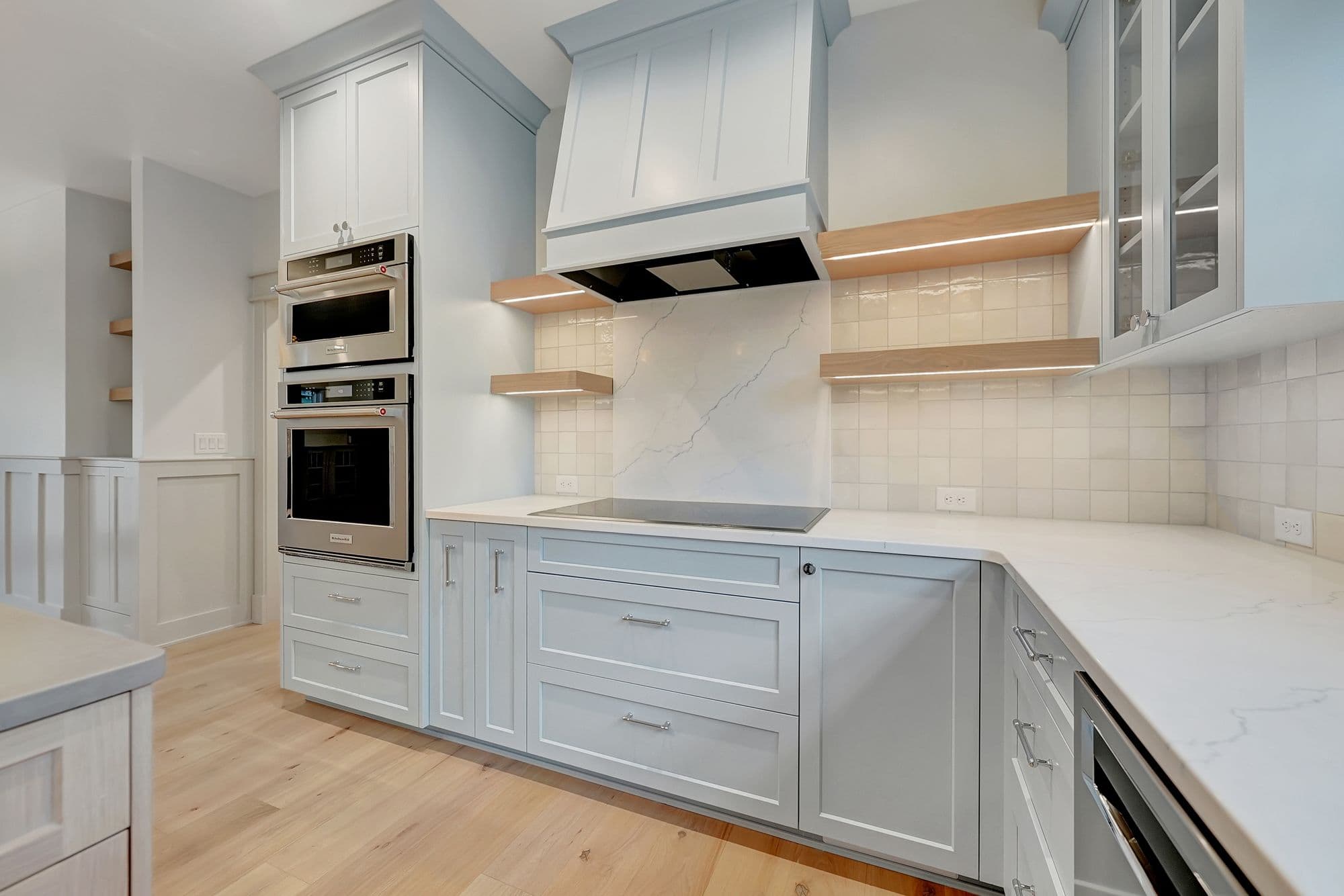 Modern kitchen with light blue cabinets, stainless steel appliances, and light wood flooring. The kitchen features a white countertop and backsplash.