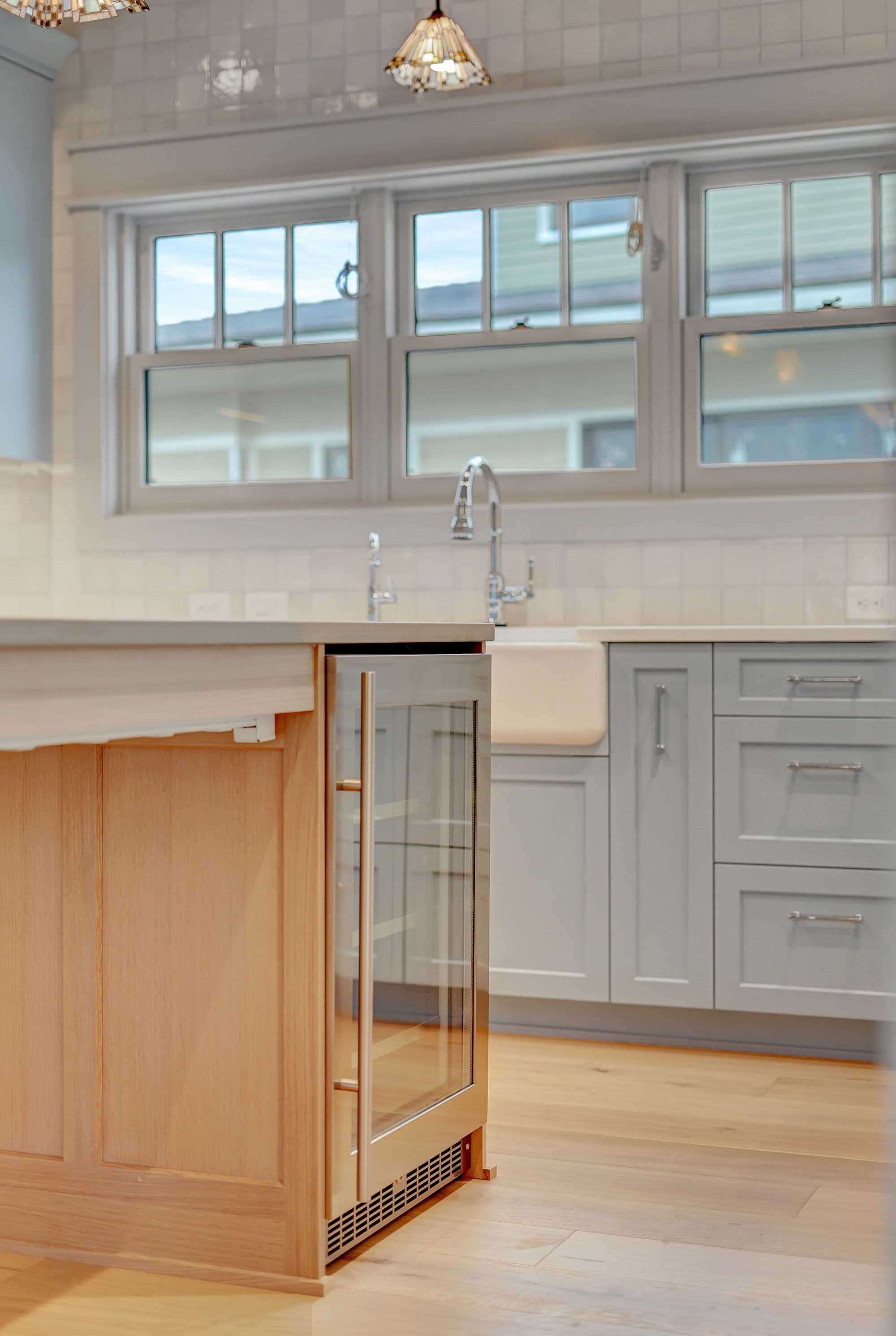 Kitchen featuring light blue cabinets, a farmhouse sink, and stainless steel appliances. Hardwood floors and a tile backsplash add warmth and texture to the space.
