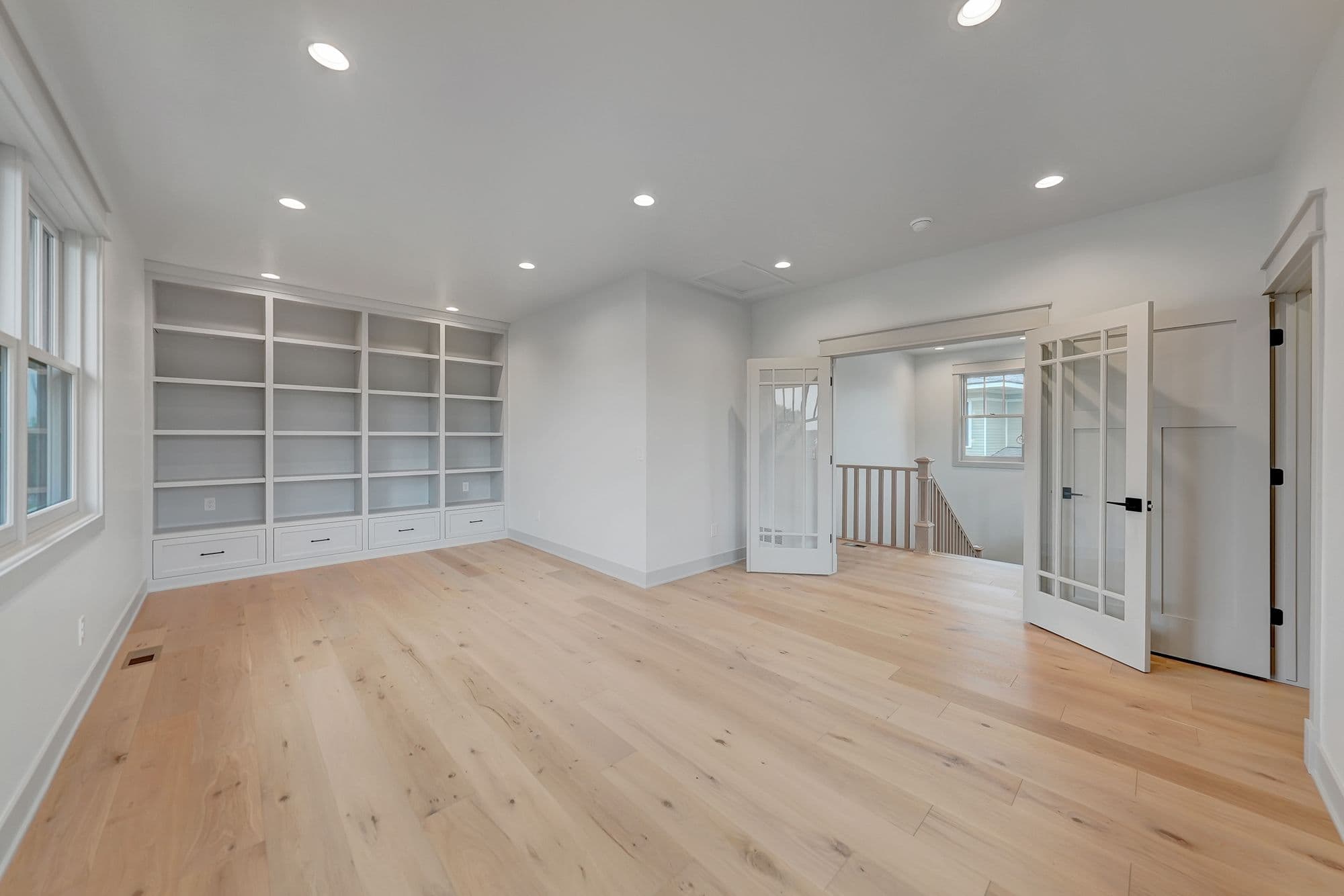 Bright and airy living room with hardwood floors and built-in shelving. The room features a set of double doors leading to a staircase.