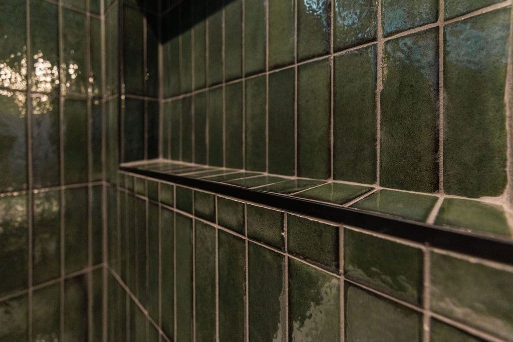 This bathroom features dark green, square-shaped tiles with light gray grout lines throughout the shower. A built-in niche shelf with a black trim sits in the shower.